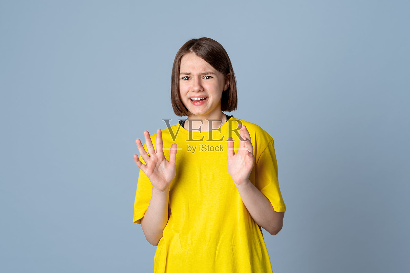 惊恐万分的少女站在浅灰色的背景上。情感、人与生活理念照片摄影图片