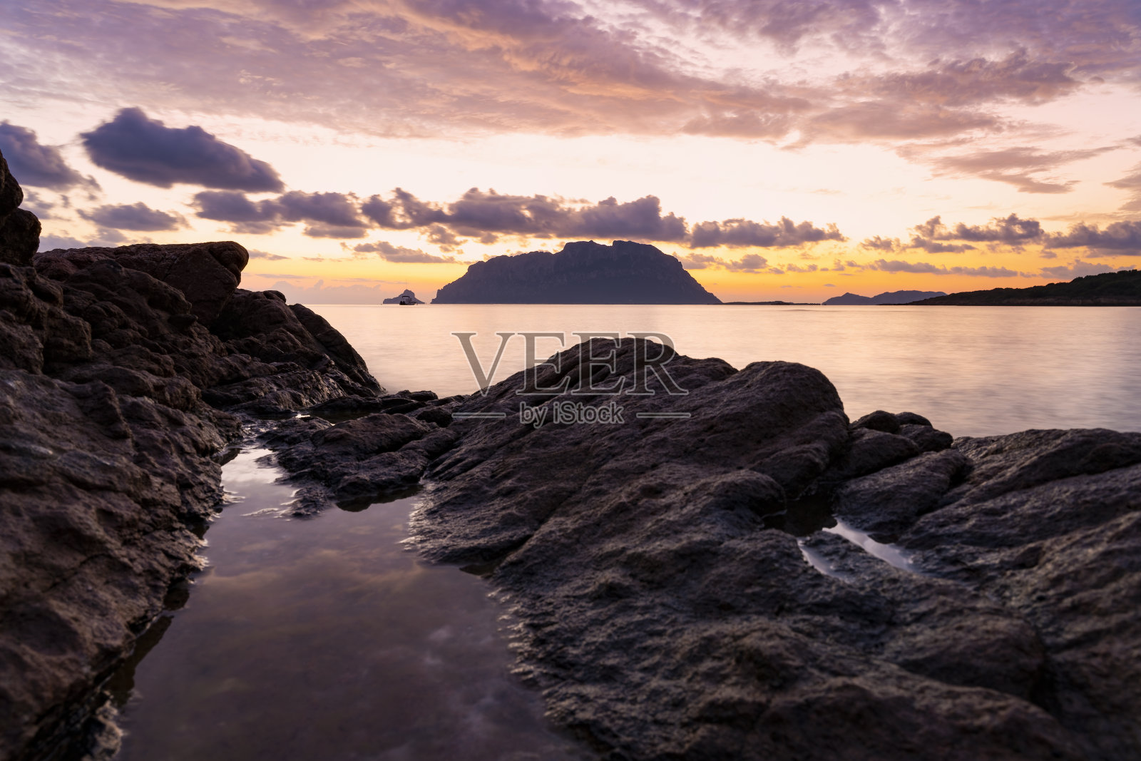 (选择性聚焦)塔沃拉拉岛惊人的剪影在一个戏剧性的日出与sonone花岗岩岩石的前景。意大利，撒丁岛，波尔图。照片摄影图片