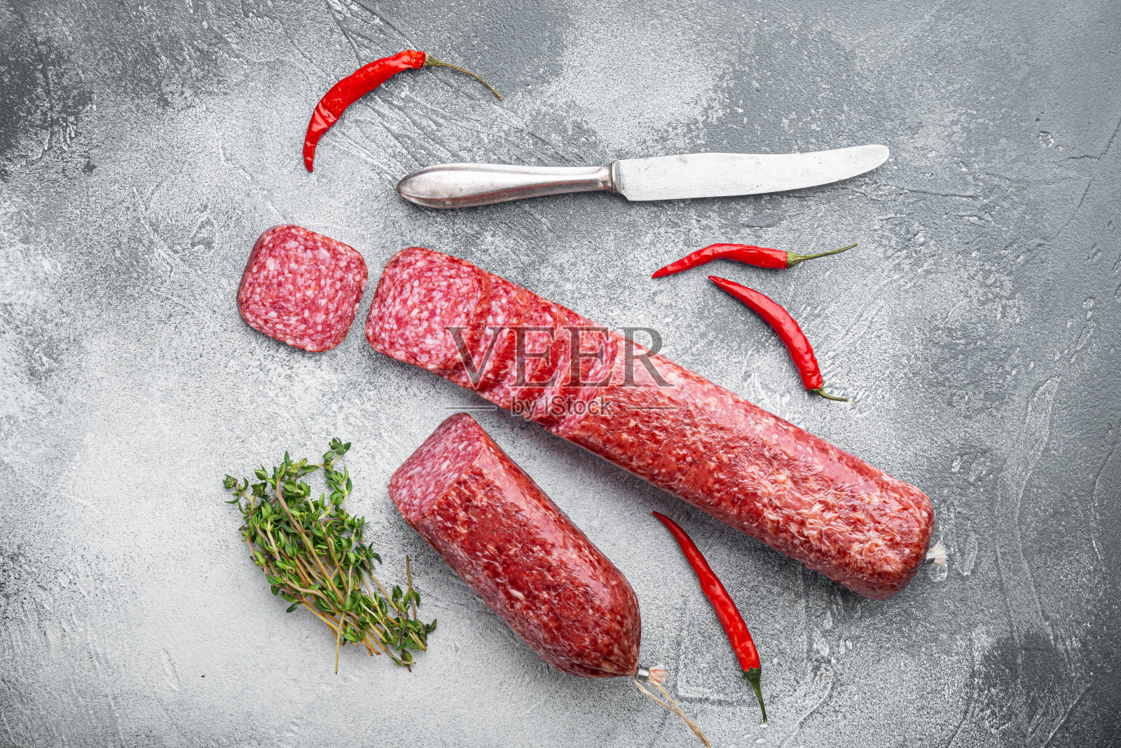 干腊肠配上新鲜的迷迭香和香料，放在灰色的石桌背景上，俯视图平铺照片摄影图片