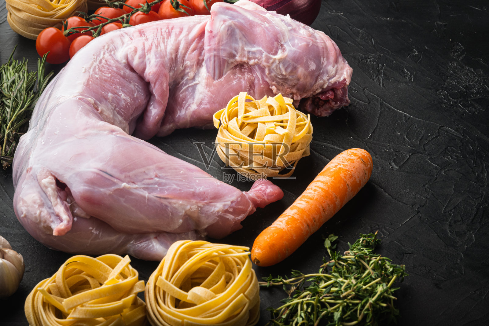 生兔肉和烹饪原料炖意大利宽面条，在黑色石头背景，复制空间的文本照片摄影图片