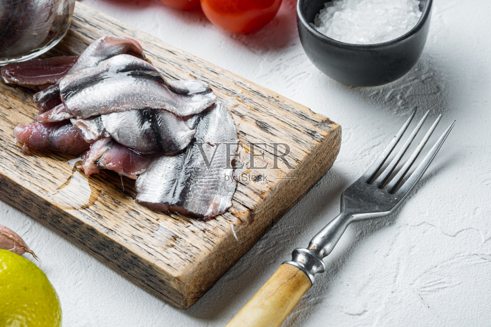 腌凤尾鱼，放在木制砧板上，白色的背景上有香草和配料照片摄影图片