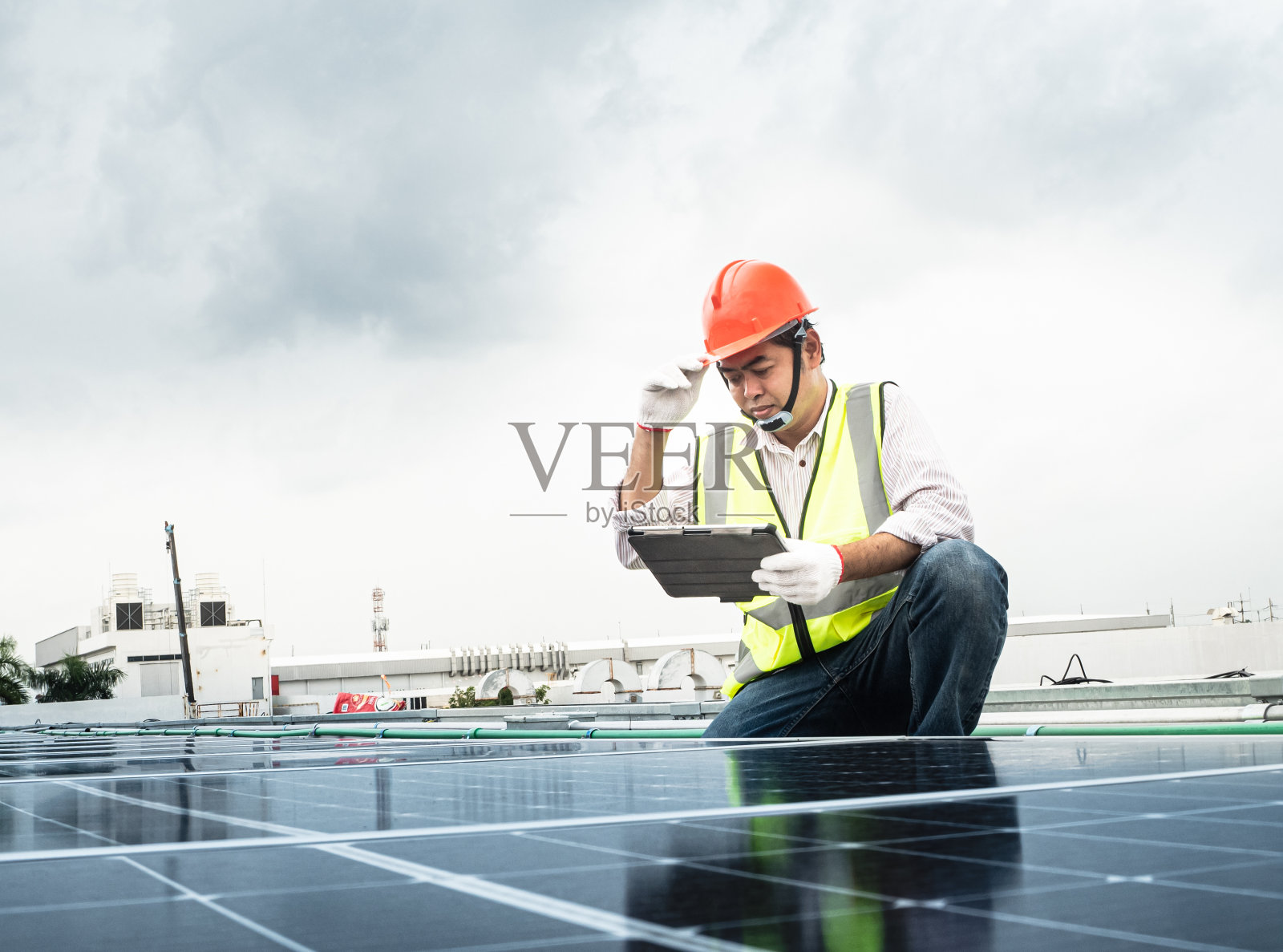 一名男工程师正在检查一个光伏(太阳能)工厂，并使用一个记录板。戴着防护头盔的机械师。穿着制服的男人拿着药片。照片摄影图片