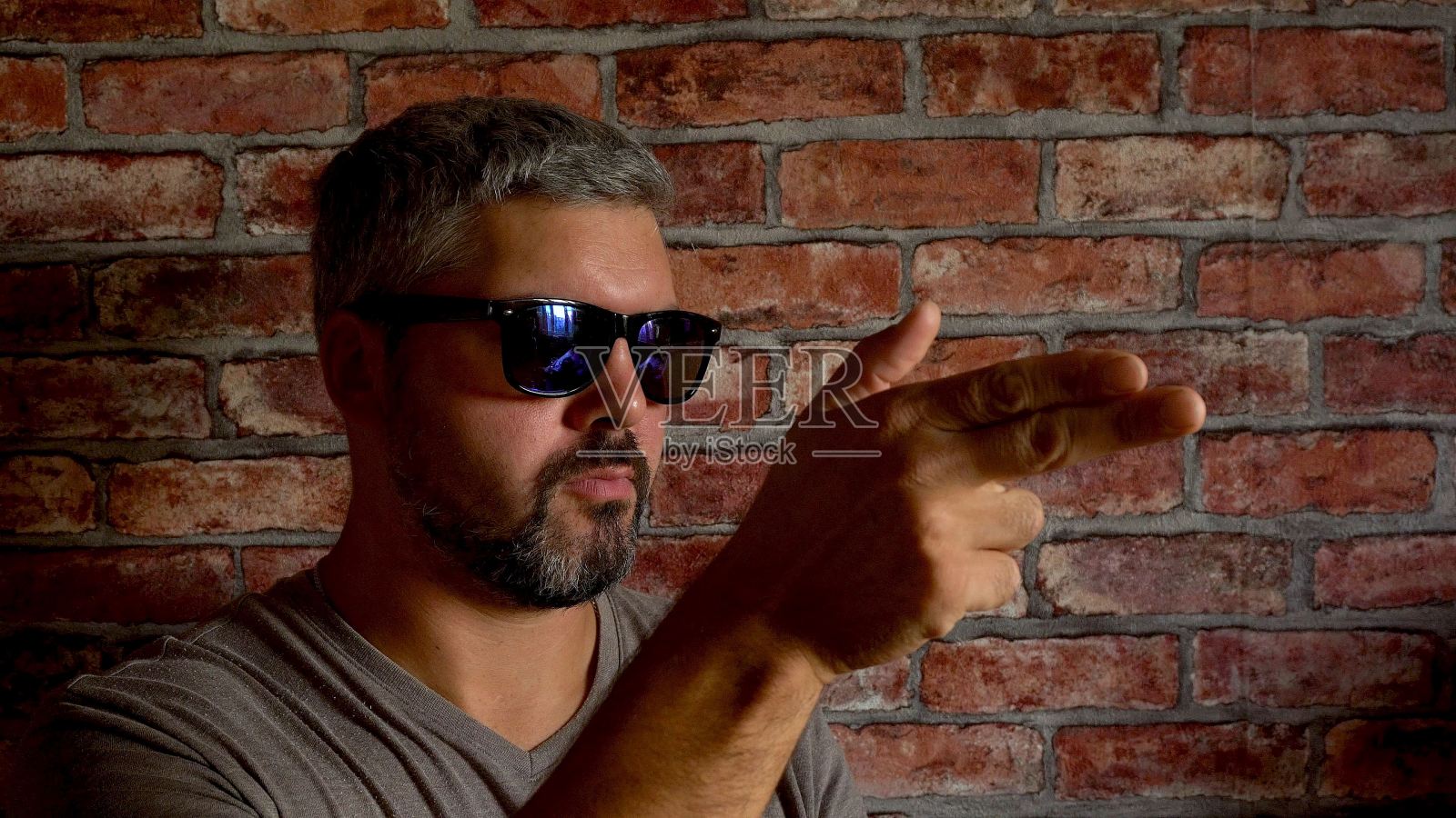 一个成年男子靠砖墙坐着。从手指射出照片摄影图片