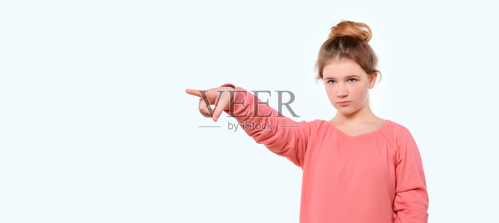 穿着粉色休闲运动衫的年轻女孩惊讶地指着复印室。站在白色的工作室背景下照片摄影图片