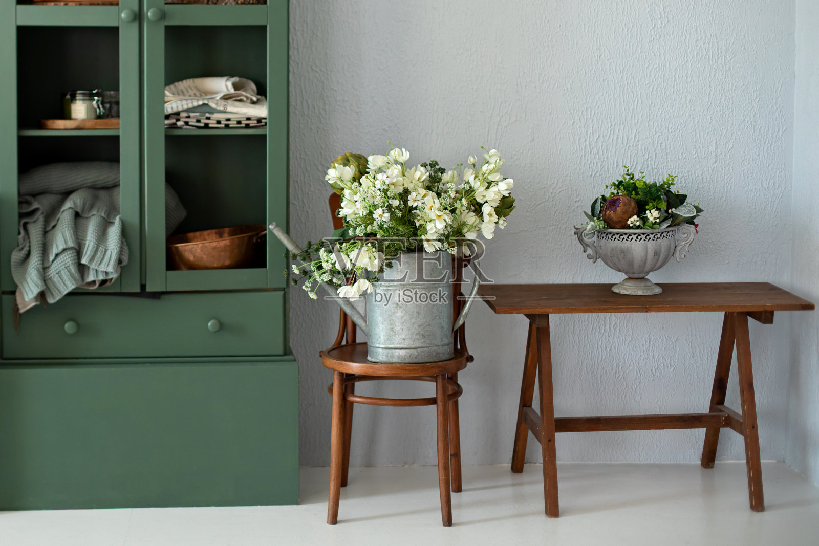 舒适的家居装饰。厨房内部有家具。橱柜旁木椅上的喷壶里有一束美丽的鲜花。园艺的概念。古典园林工具。花插在花瓶里的时髦美食照片摄影图片