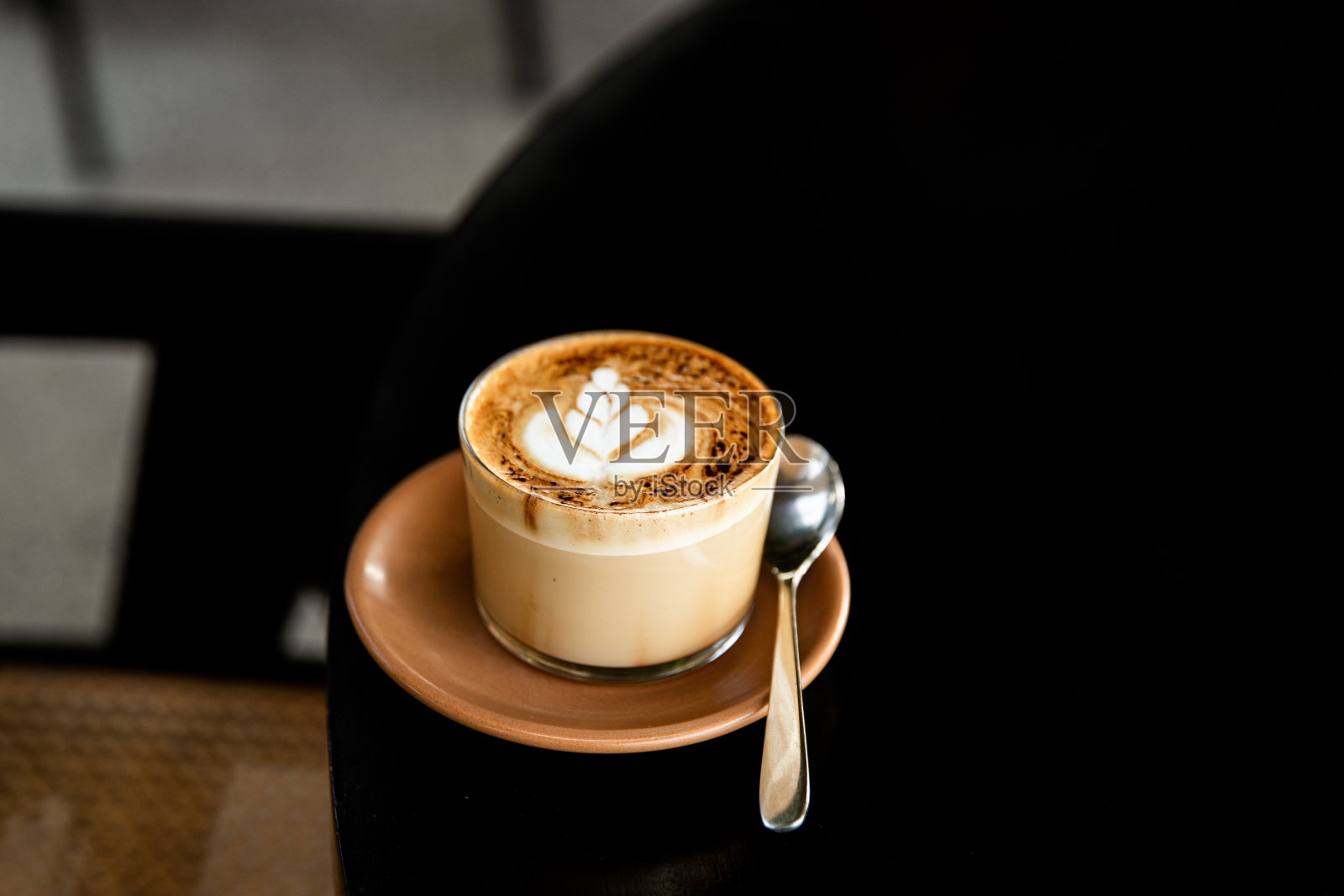 杯卡布奇诺，茶托上有拿铁图案，黑色的桌子上有勺子照片摄影图片