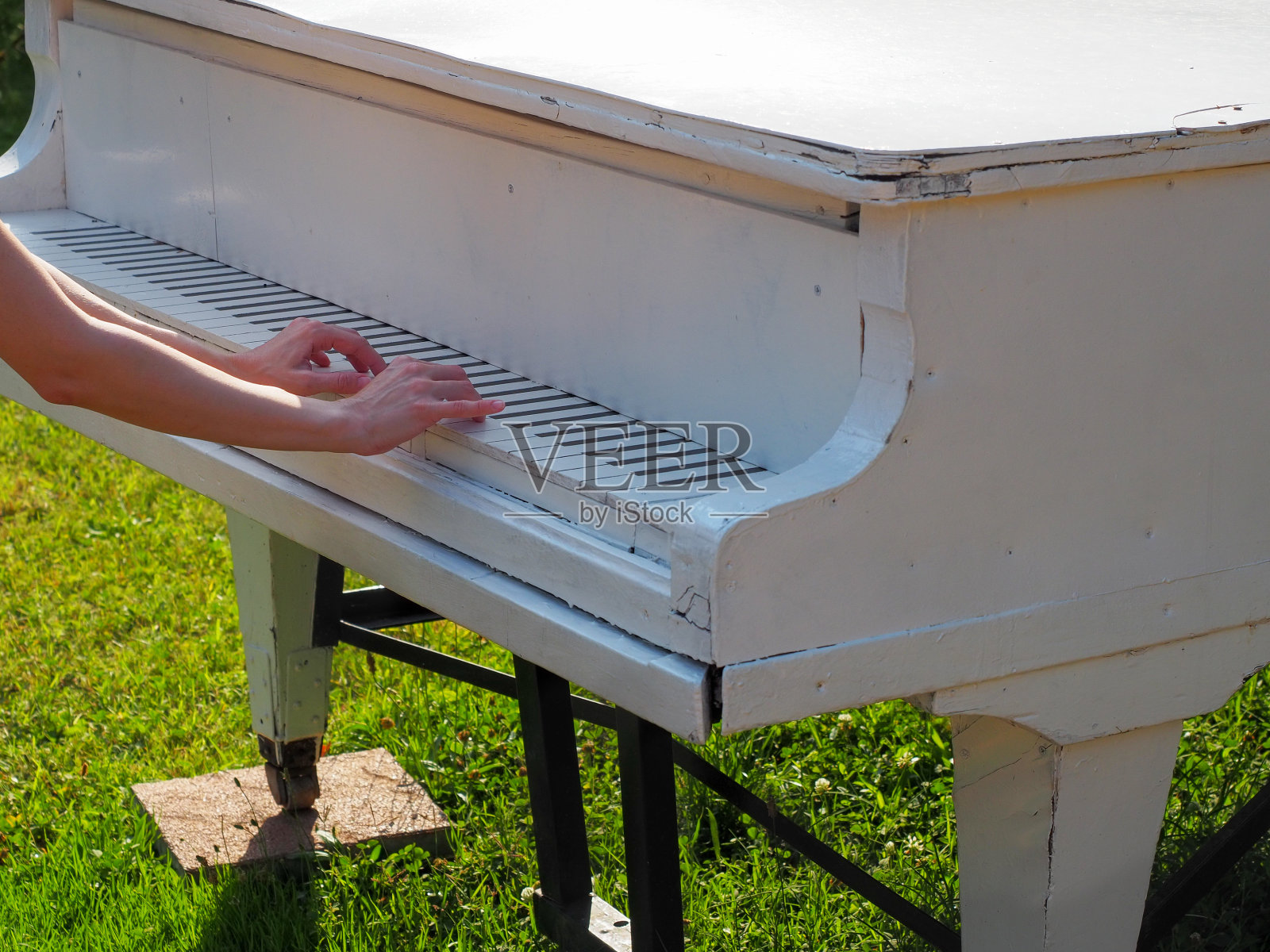 在公园的绿色草坪上，女人们的手放在一架旧白色三角钢琴的假键盘上。钢琴的片段照片摄影图片