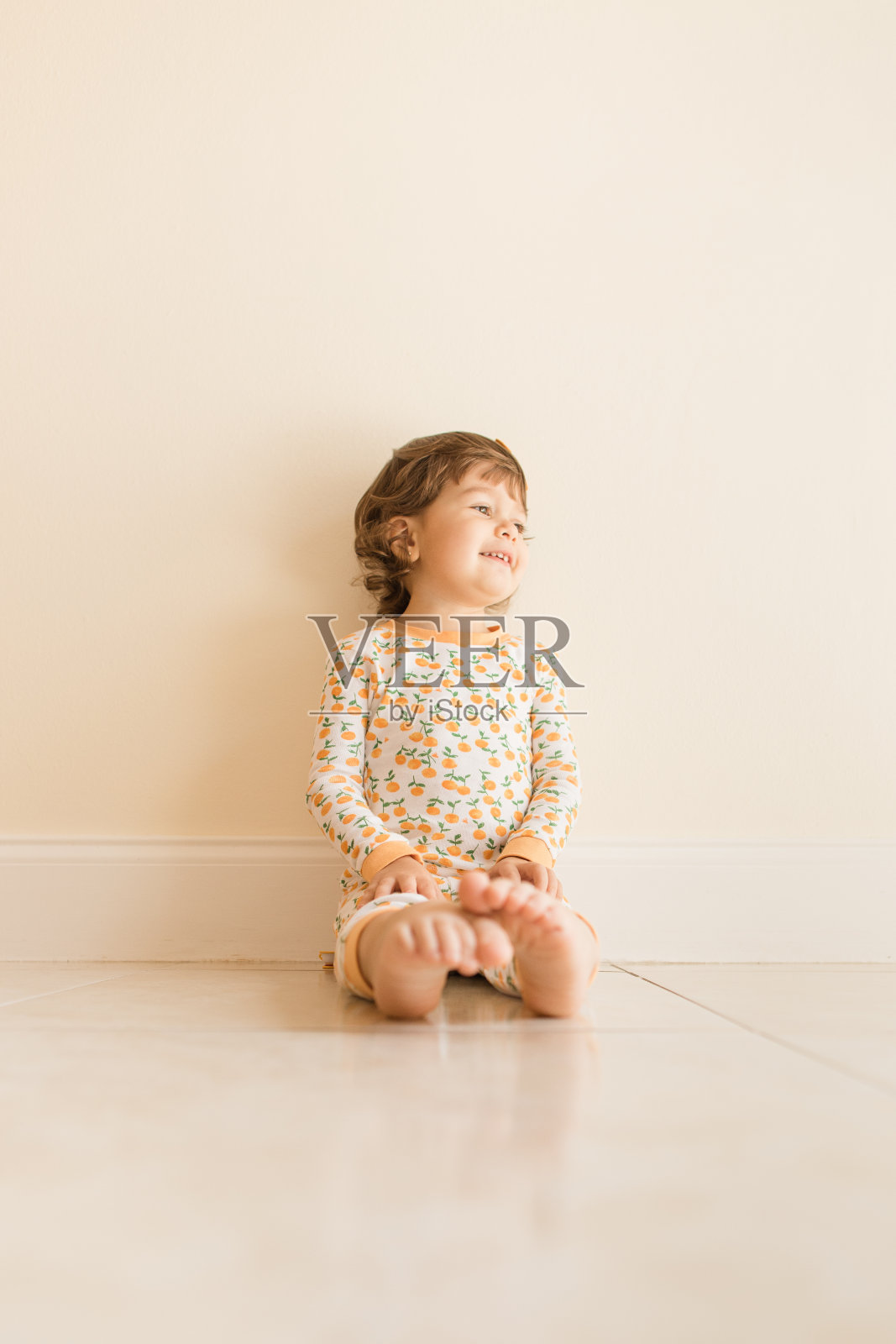 2021年9月，两岁的小女孩坐在地板上玩和吃橘子，穿着橙色睡衣和橙色的头发蝴蝶结在家里照片摄影图片