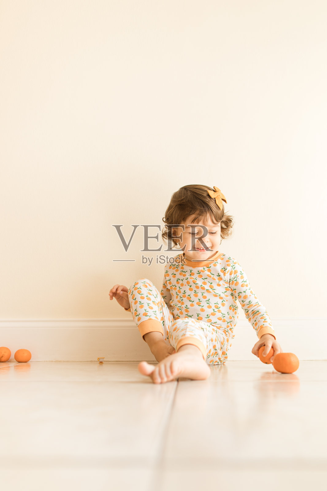 2021年9月，两岁的小女孩坐在地板上玩和吃橘子，穿着橙色睡衣和橙色的头发蝴蝶结在家里照片摄影图片