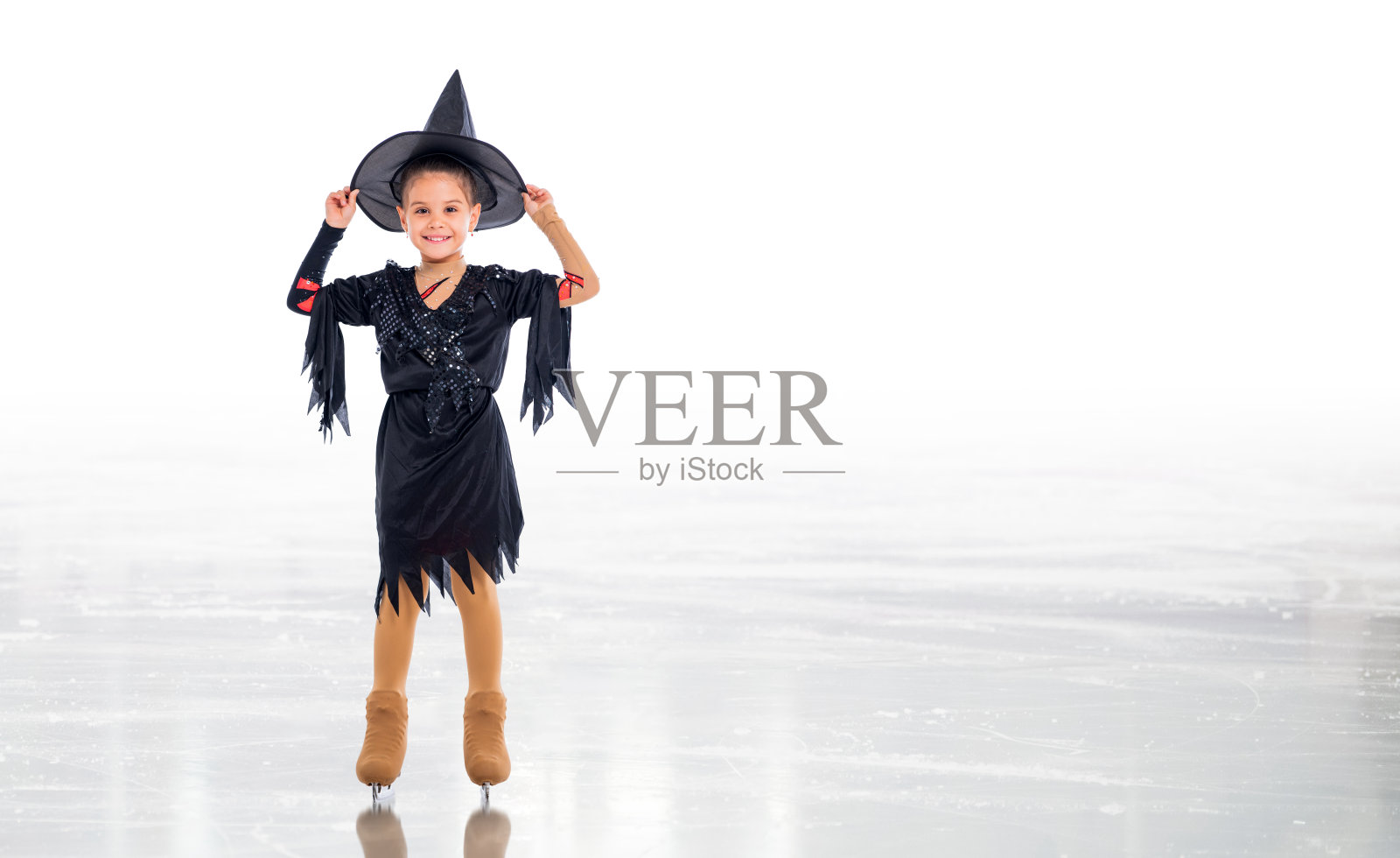穿着女巫服装的小溜冰者在白色背景的冰上为万圣节摆姿势照片摄影图片