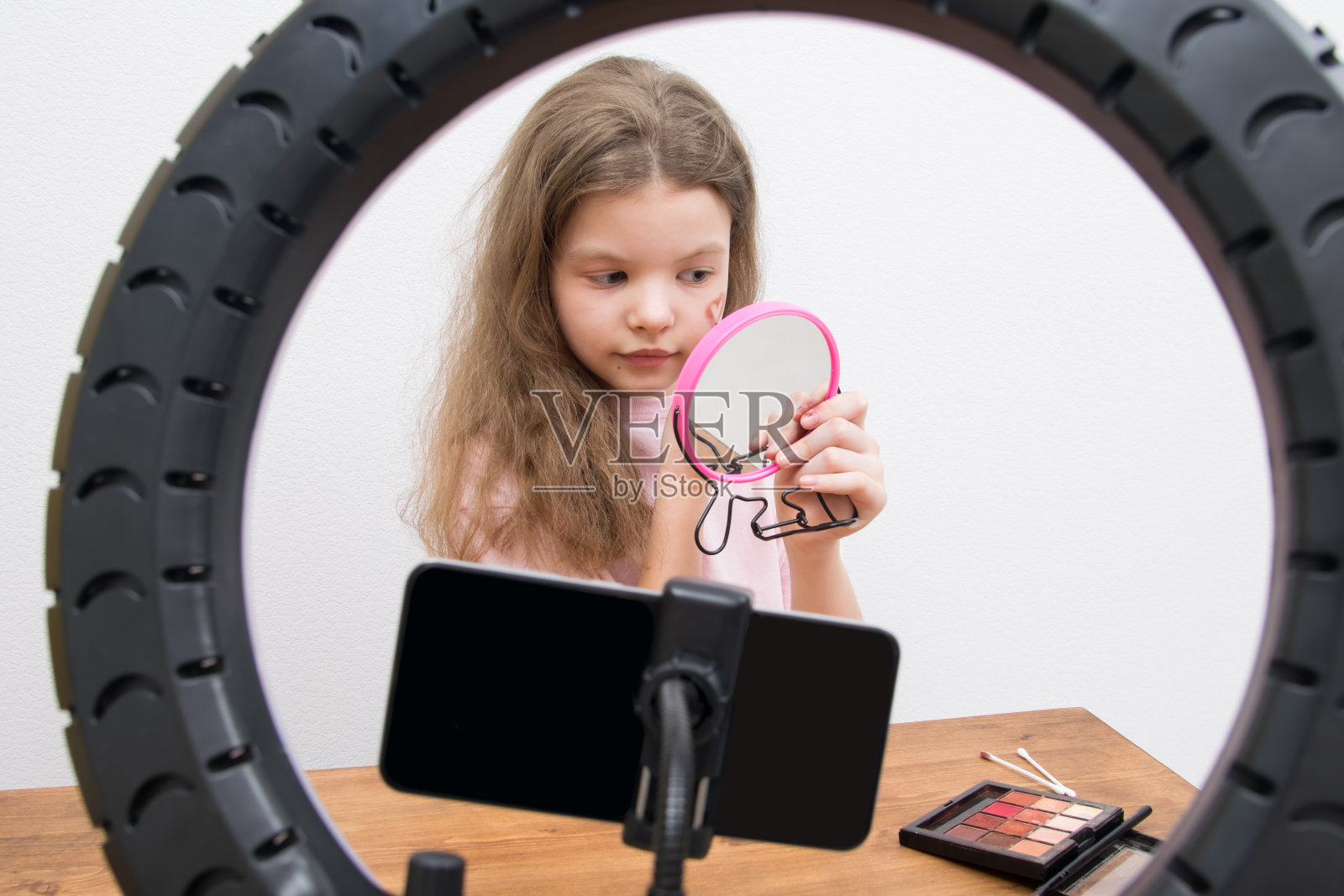 在一盏圆形灯和一部智能手机的中央，一个写博的女孩正在化妆，在她的脸颊上画了一颗心照片摄影图片