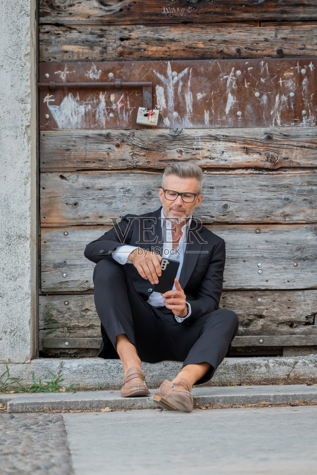 一个英俊的年轻商人坐在楼梯上用他的智能手机。
企业家在公园工作，坐在楼梯上用手机发短信照片摄影图片