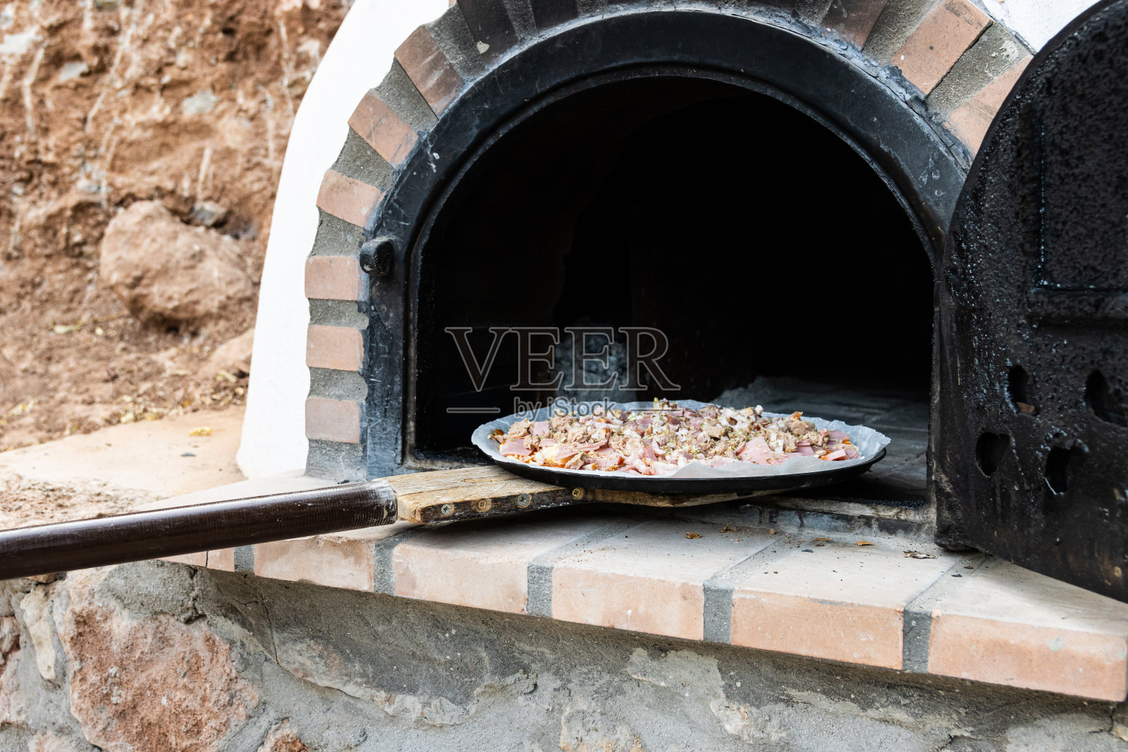 一名男子正在用铁锹把披萨放进户外手工烤炉里照片摄影图片