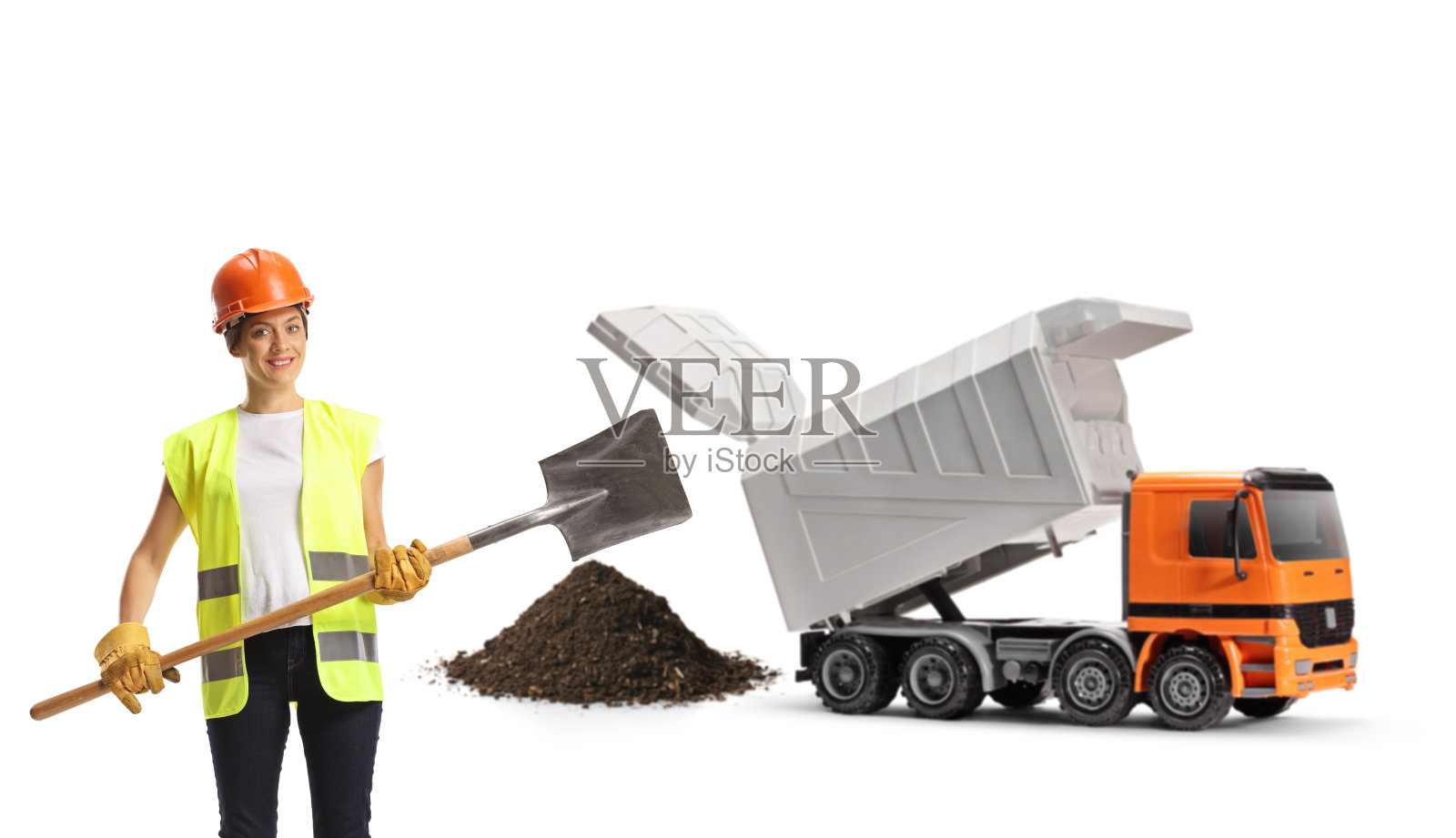 女建筑工人，穿着背心，戴着安全帽，拿着铁锹站在自卸卡车前照片摄影图片