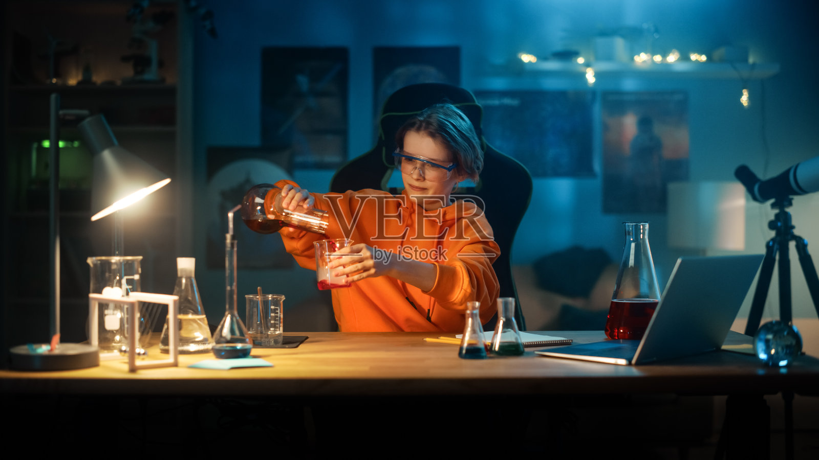 在安全眼镜里的聪明小男孩在家里的烧杯里混合化学物质。青少年进行教育科学兴趣实验，在他的房间里做有趣的生物作业。照片摄影图片