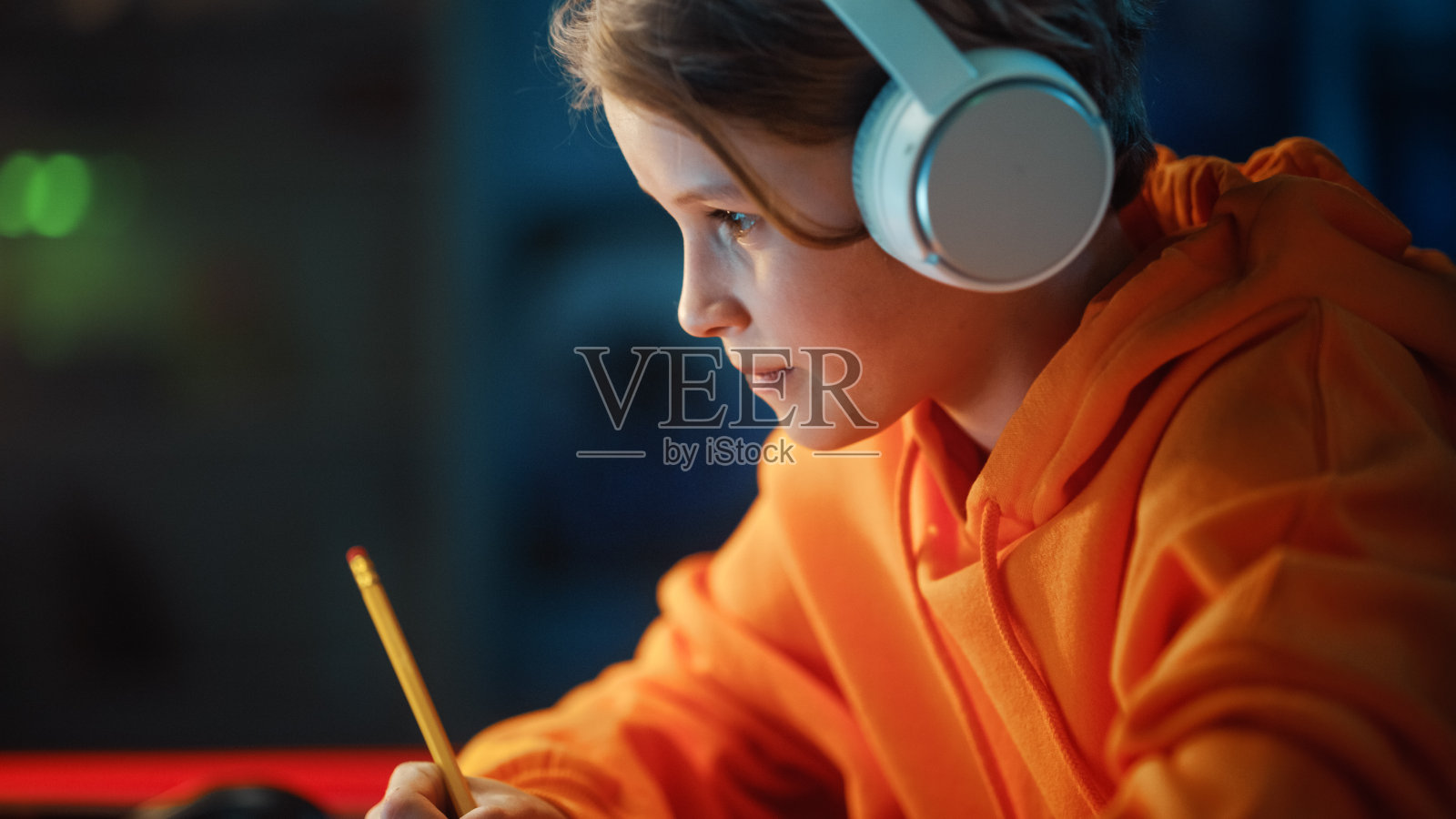 聪明的小男孩戴着耳机在舒适的黑暗房间里用笔记本电脑参加在线课程。快乐的青少年浏览在线教育研究，在笔记本上写作，学习学校作业。照片摄影图片