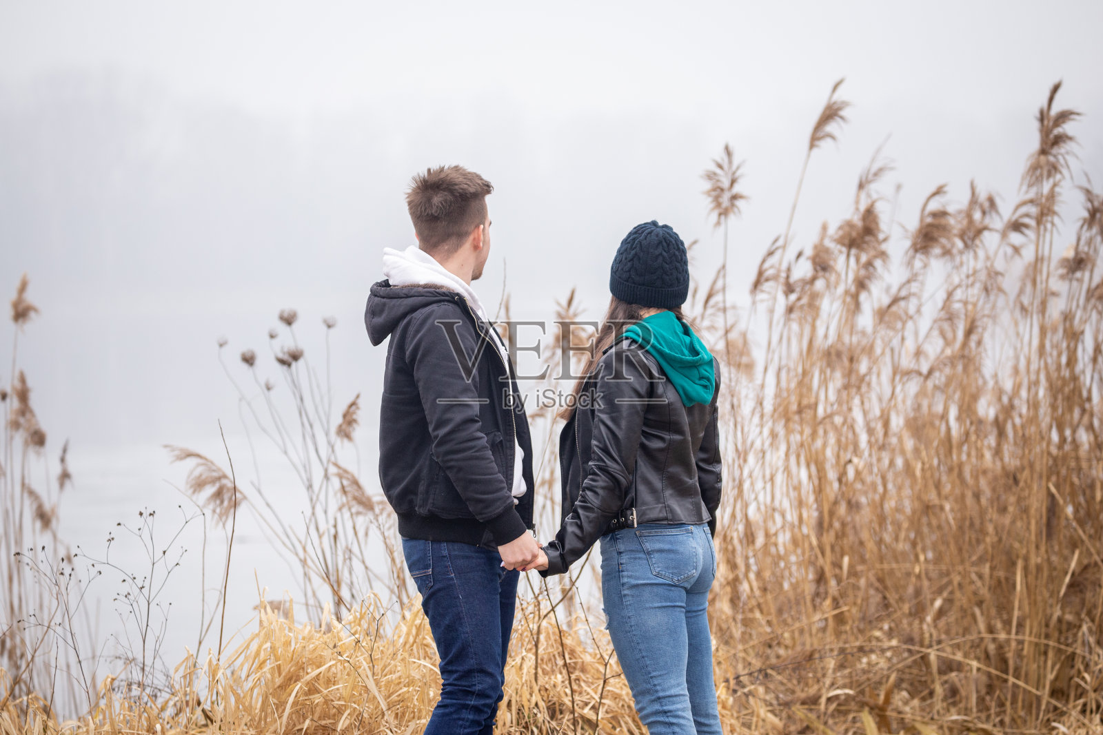 在一个雾蒙蒙的冬日，一对年轻夫妇站在湖边照片摄影图片