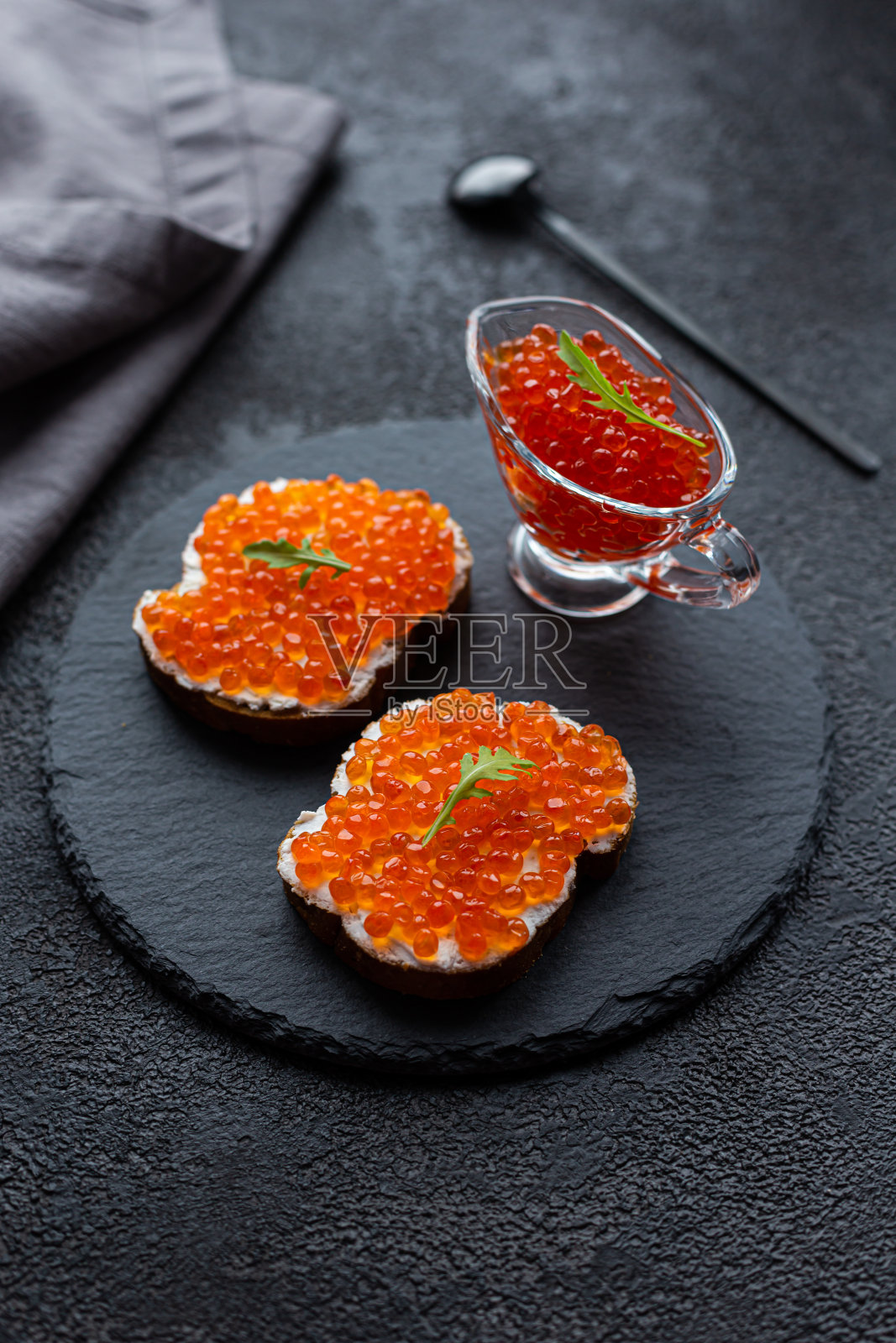 碗里放着红鱼子酱，黑色石板上放着鱼子酱三明治照片摄影图片