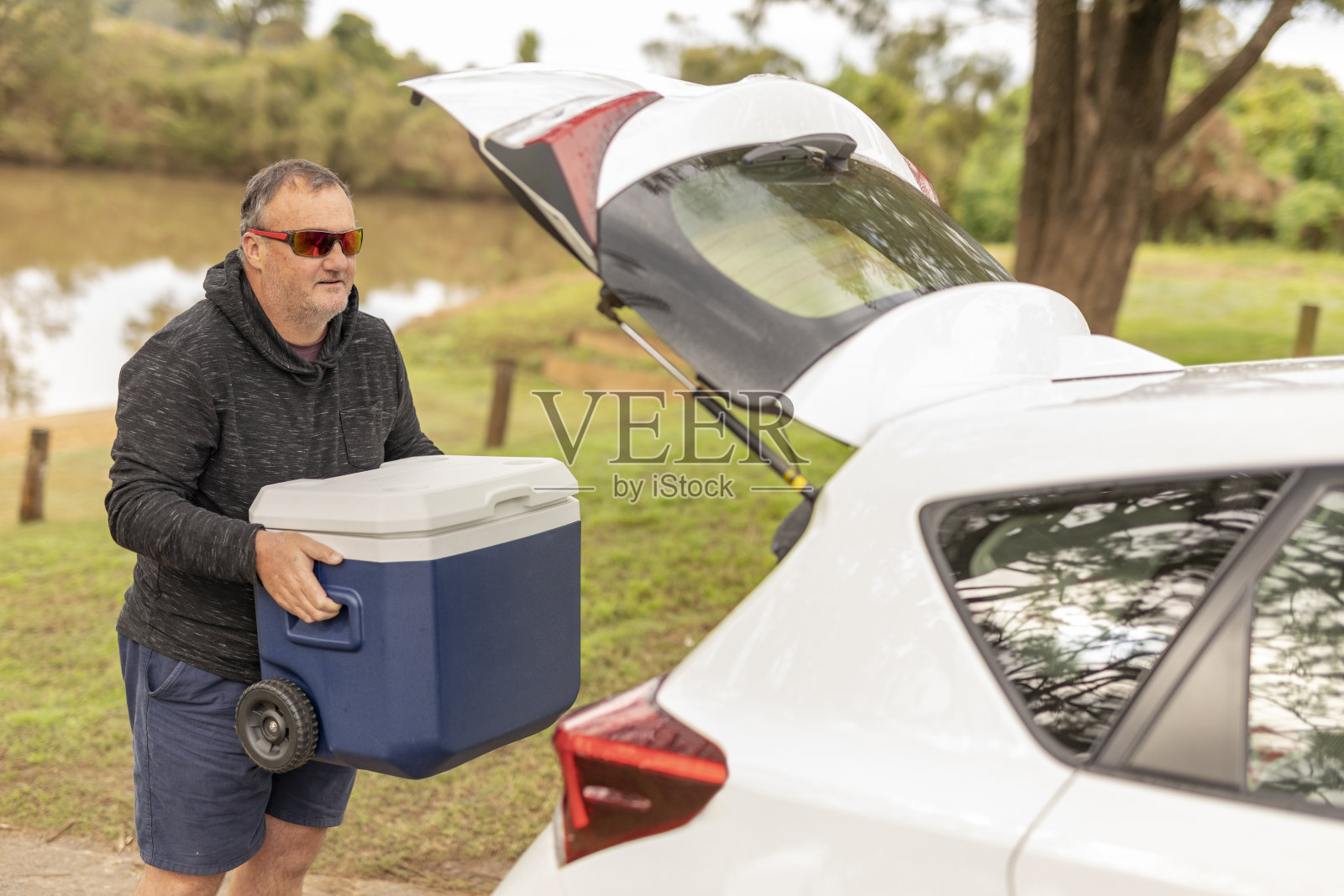 一个中年男人带着他的车和一个冷却器在河边照片摄影图片