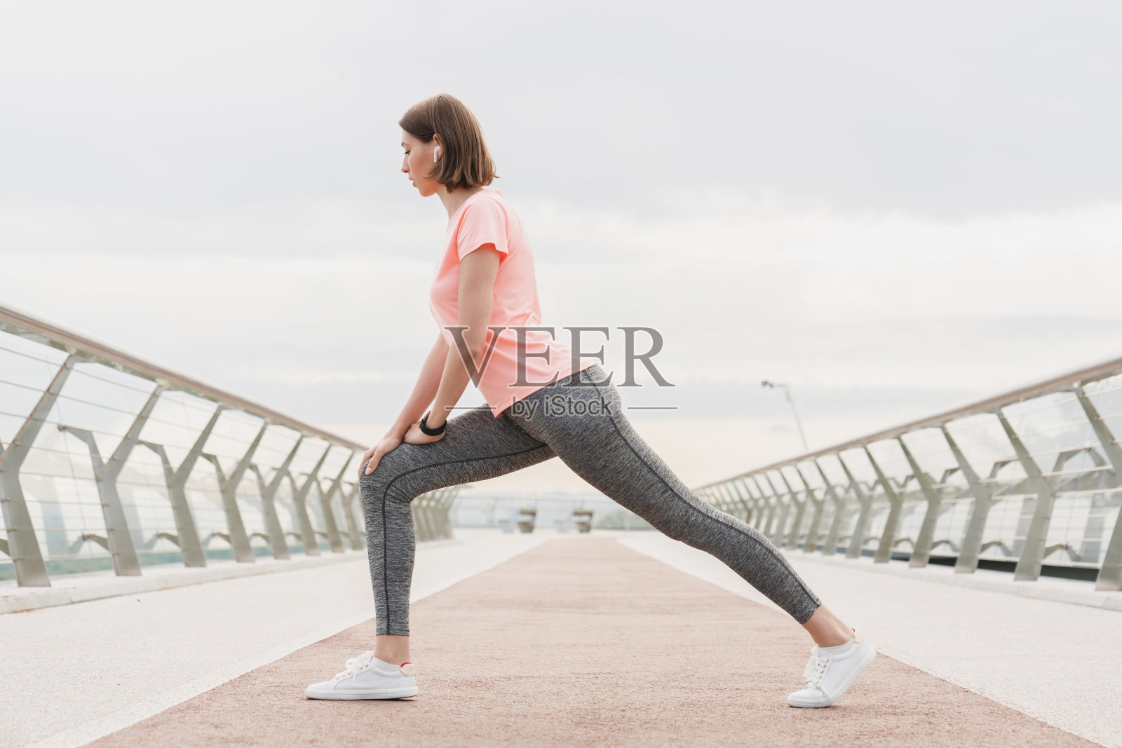 健美的年轻白人女运动员，女运动员慢跑者在城市城市桥上跑步前伸展，穿着健美的衣服，在户外训练前做练习。照片摄影图片