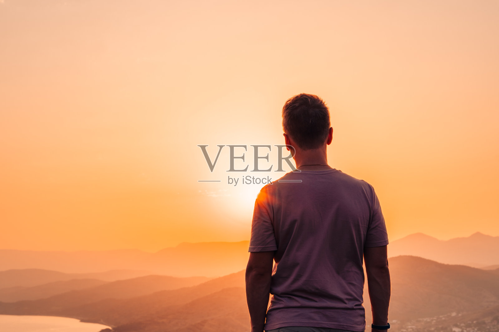 夕阳西下时，一个年轻人站在悬崖边，欣赏着令人难以置信的山景照片摄影图片