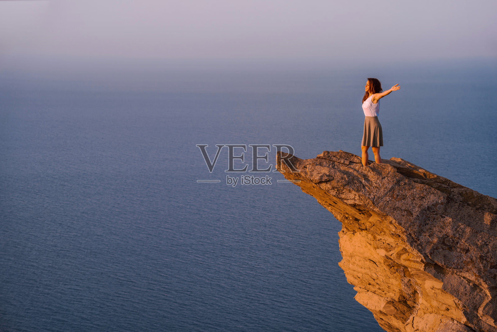 年轻女人站在海边悬崖上照片摄影图片