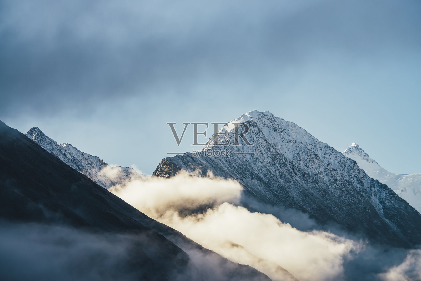 阳光下，雪山在厚厚的云层上的美丽景色。风景秀丽的山景，白雪皑皑的山峰之间密密的低云蓝天。美丽的雪峰风景。照片摄影图片