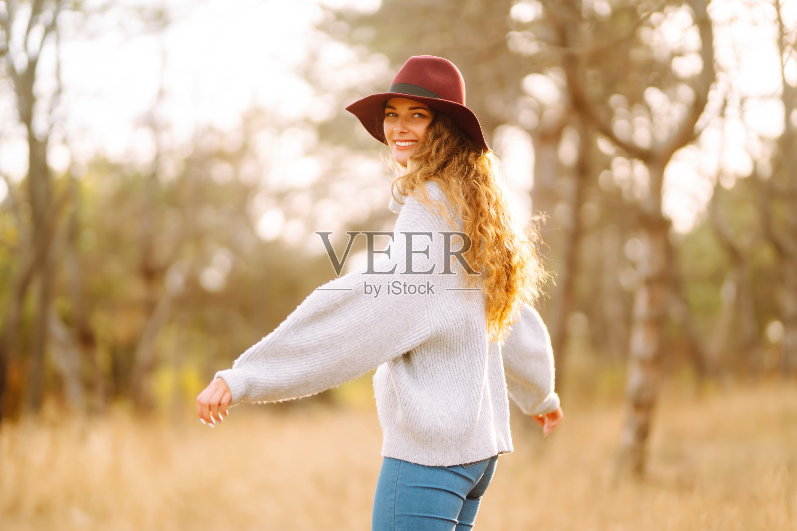 一个穿着毛衣、戴着帽子的年轻女子在公园里享受秋日。照片摄影图片