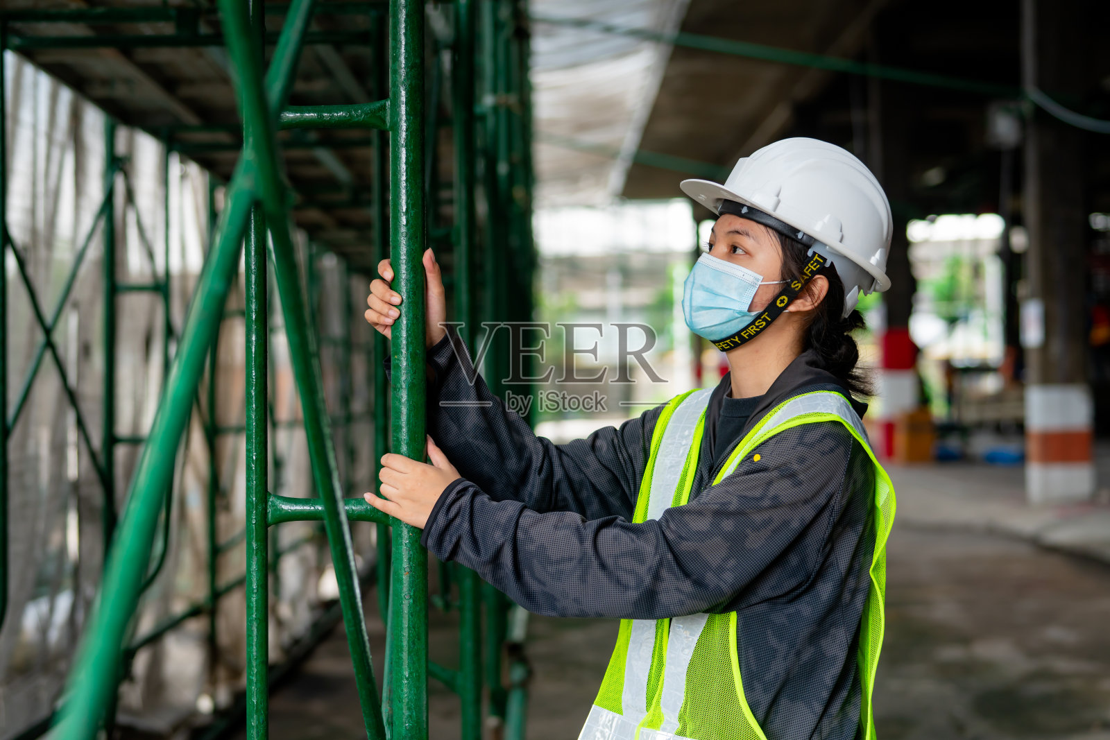 年轻的亚洲女工程师戴着医用口罩和白色安全帽，正在检查建筑区内的钢架结构照片摄影图片