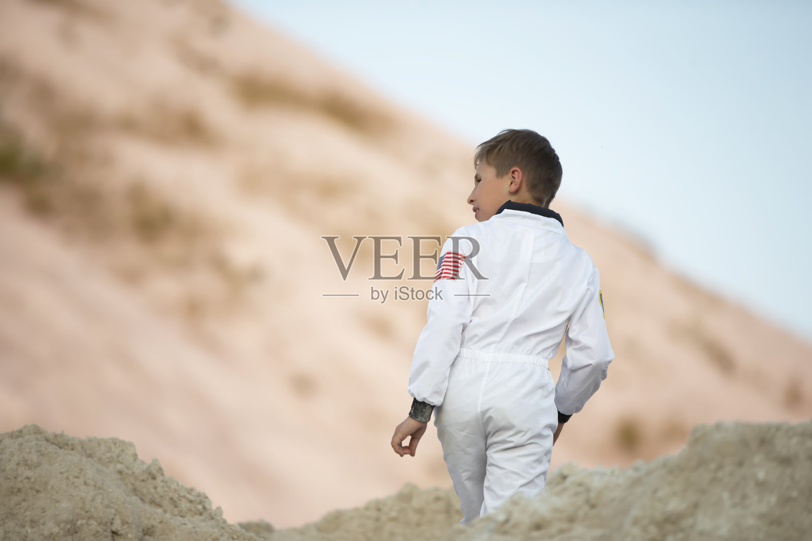 一个装扮成美国宇航员的小男孩走过异域风情的白沙山脉。照片摄影图片