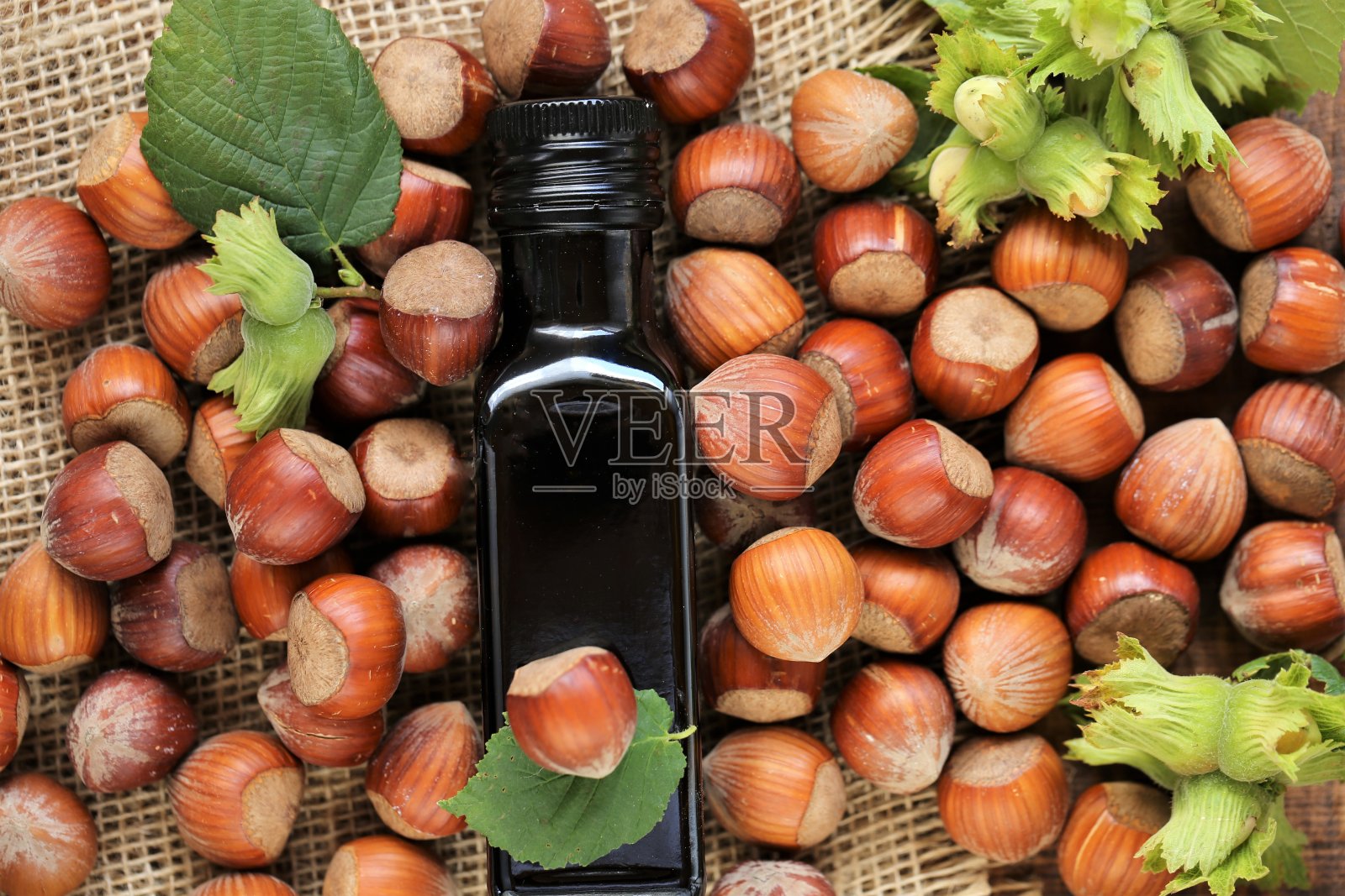 榛子油。深色玻璃瓶和榛子，绿色叶子在粗麻布上。有机素食新鲜榛子油。照片摄影图片