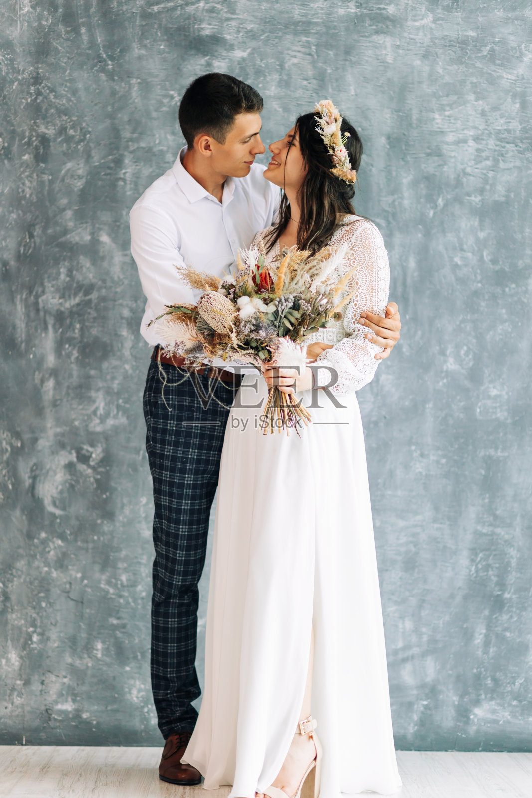 新婚夫妇在摄影棚拍摄婚纱照，幸福的年轻夫妇新娘和新郎看着对方在孤立的灰色古着墙背景照片摄影图片