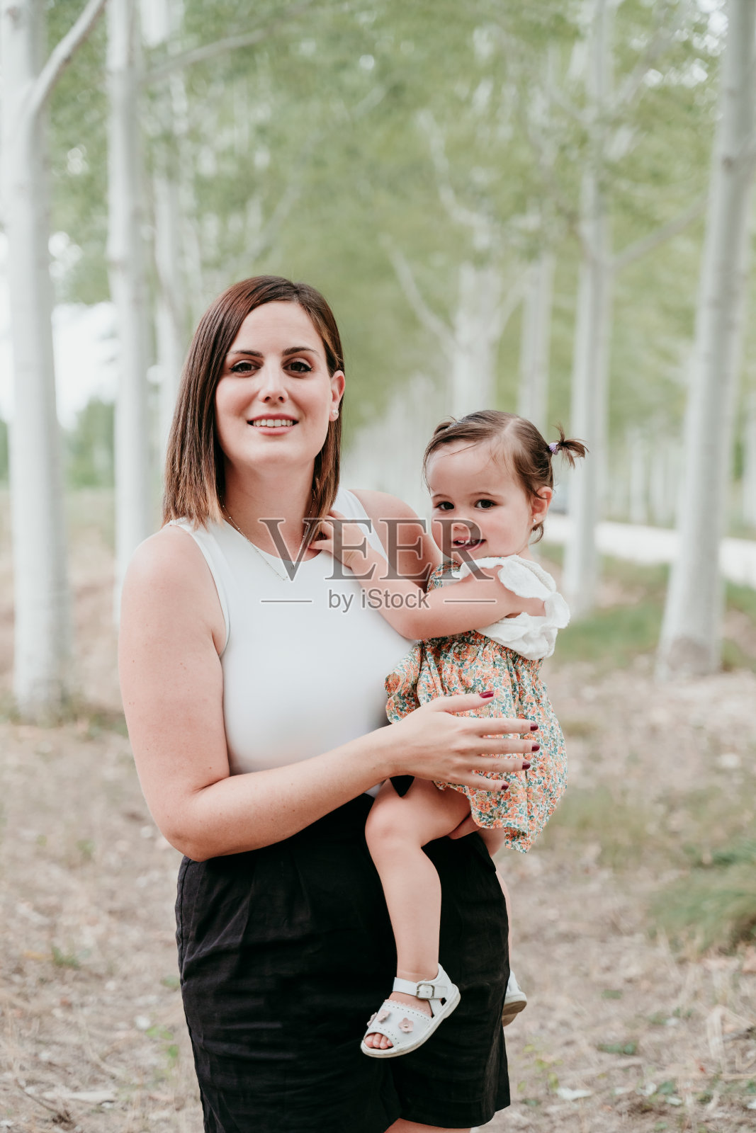 美丽的母亲抱着小女孩的画像在树的小路上。家庭、乐趣和自然的概念照片摄影图片