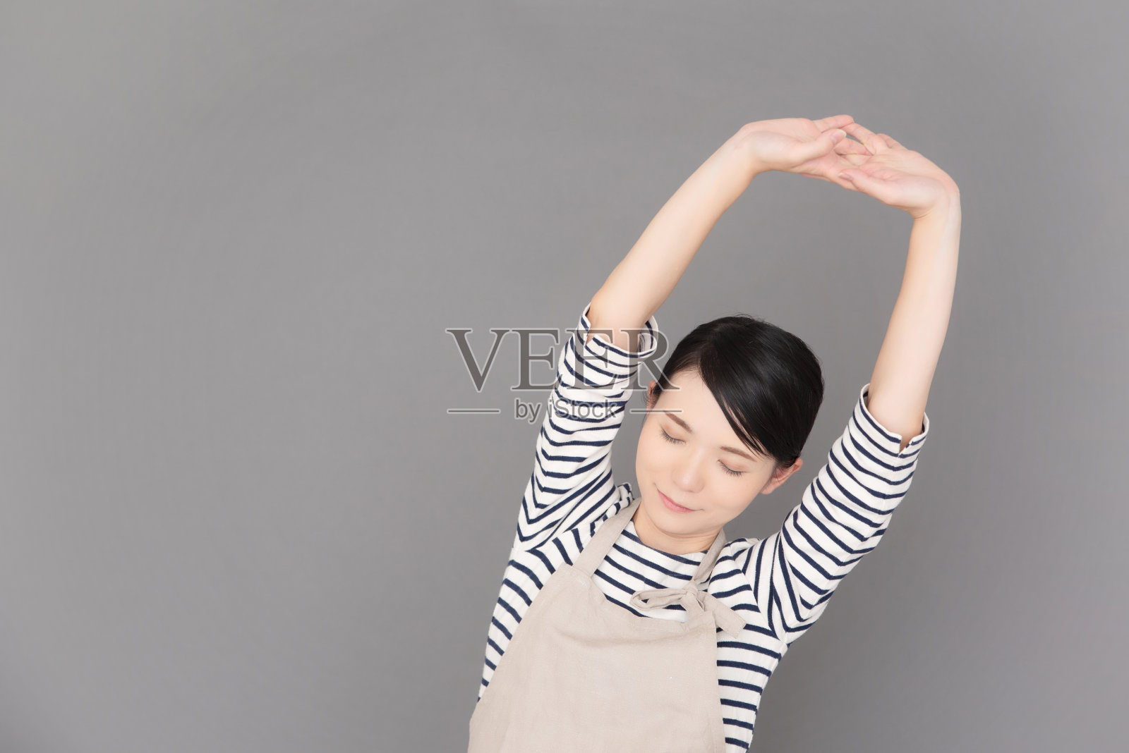 一个穿着围裙的女人站在灰色背景前照片摄影图片