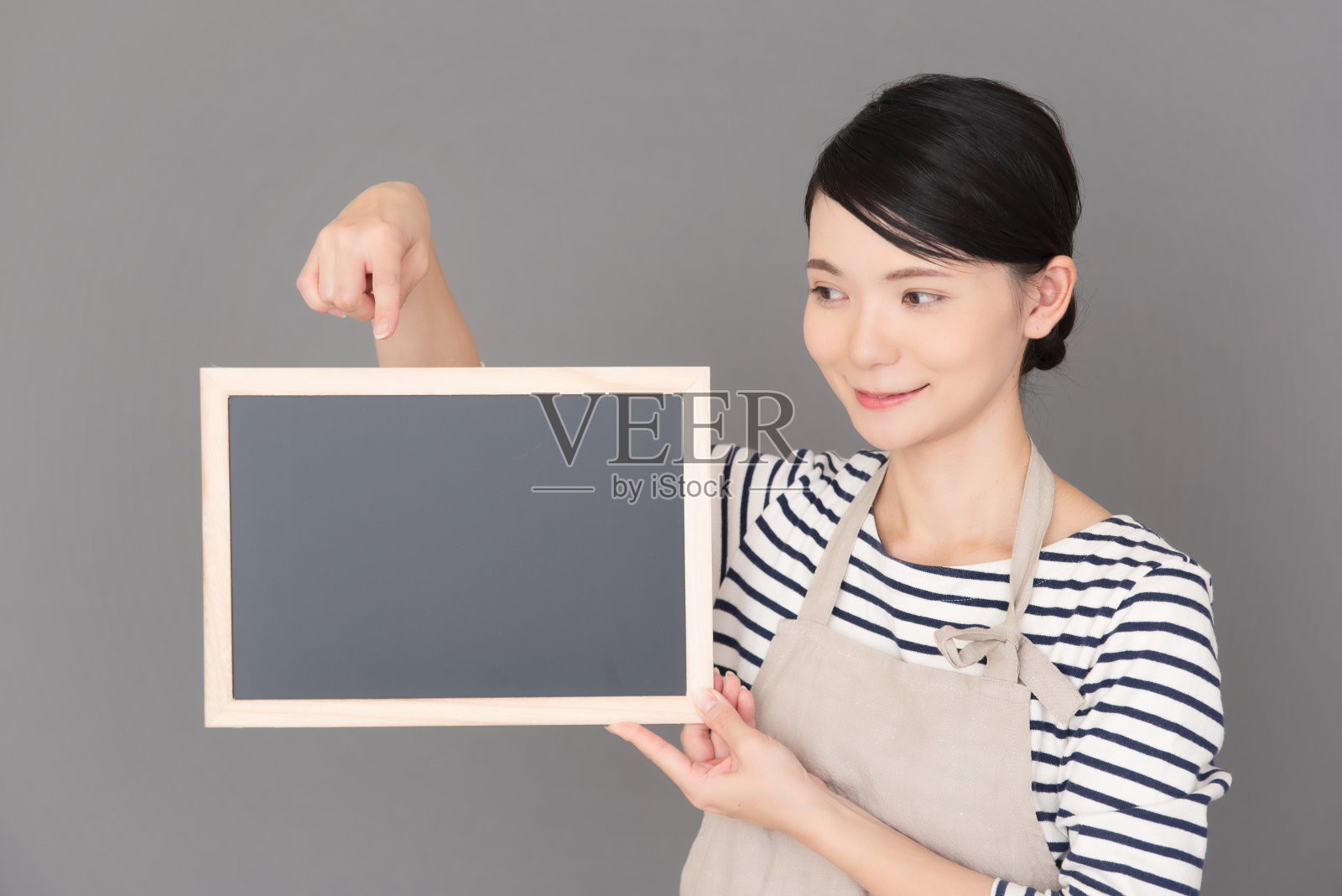 一个穿着围裙的女人站在灰色背景前照片摄影图片