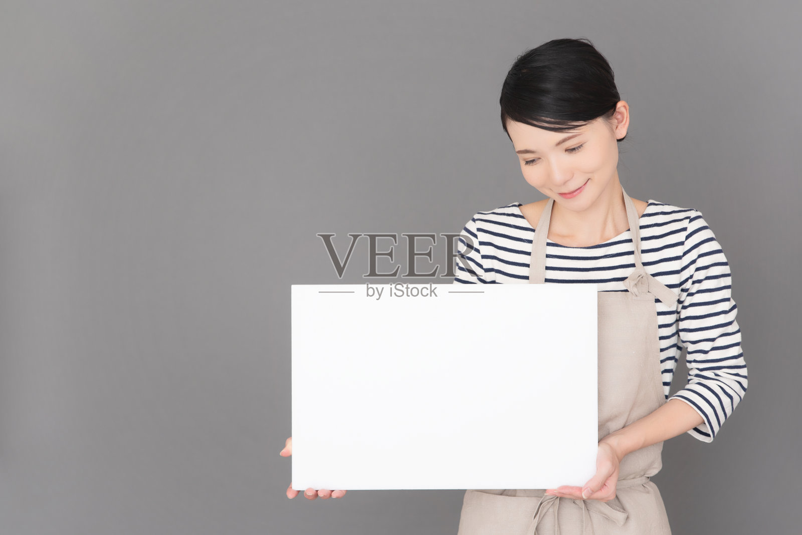 一个穿着围裙的女人站在灰色背景前照片摄影图片