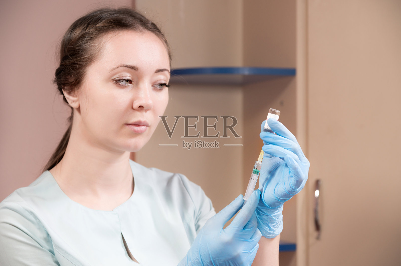 一名年轻的白人美容师的美容肖像，在温暖的背景下，手里拿着注射器。肉毒杆菌和透明质酸注射照片摄影图片