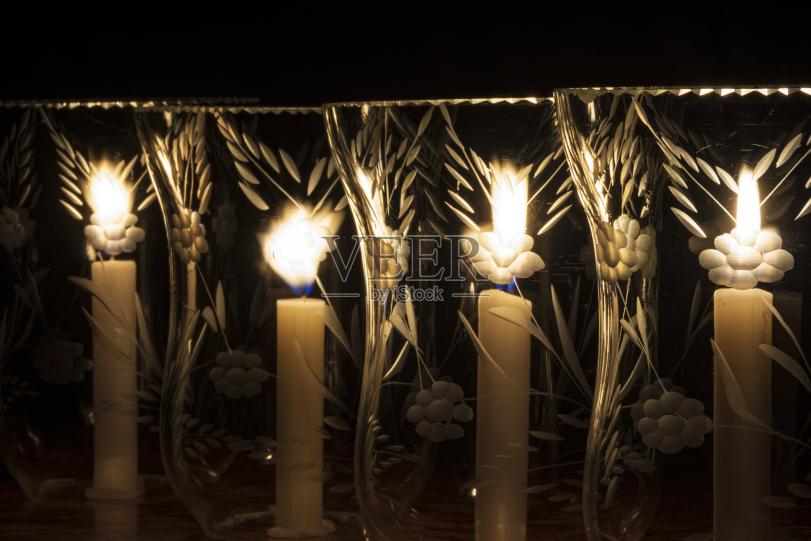 四只点燃的蜡烛插在水晶郁金香里，排成一行，从前面看照片摄影图片