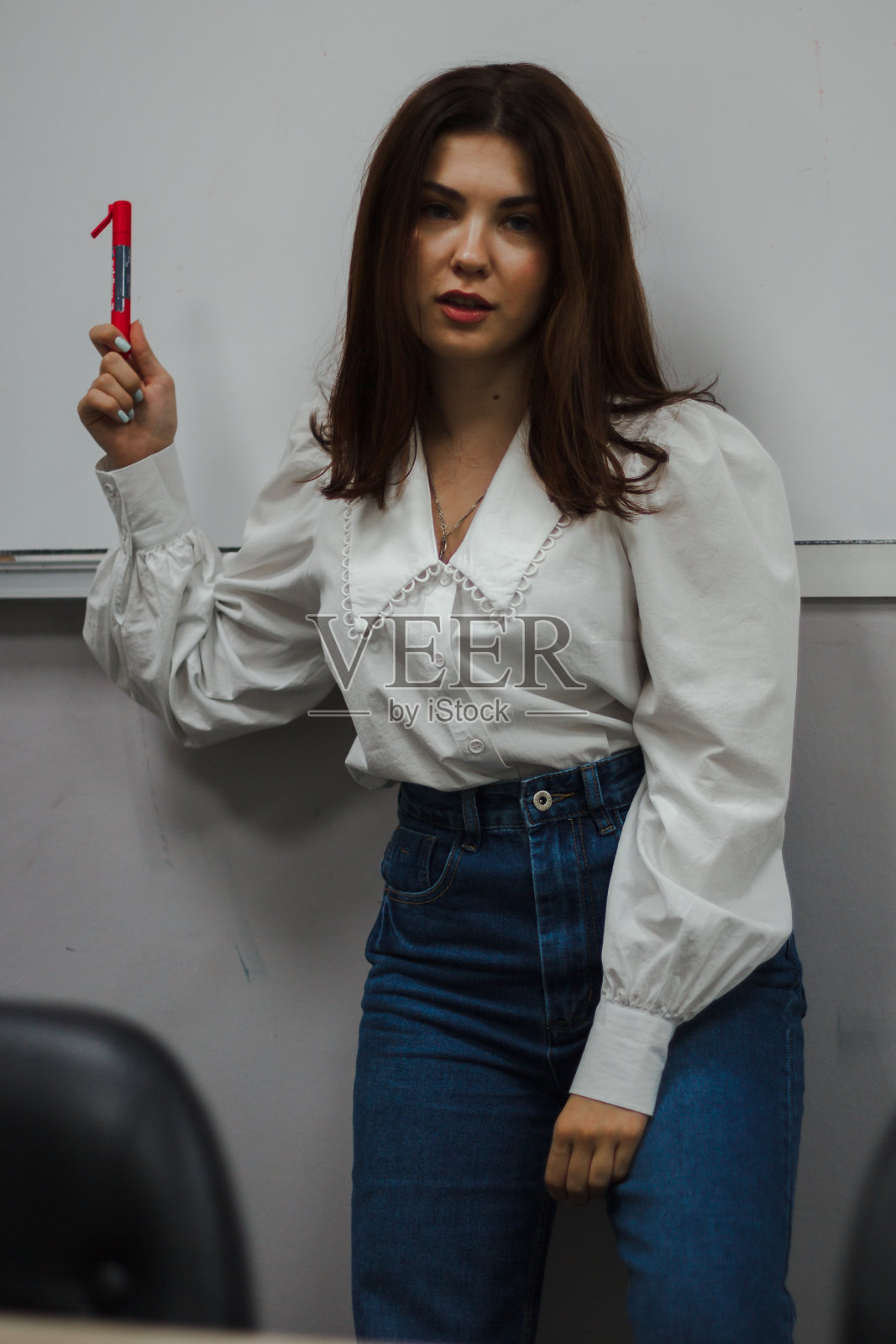 年轻的教育者穿着白色上衣，拿着红色记号笔站在白板前。看着摄像机照片摄影图片