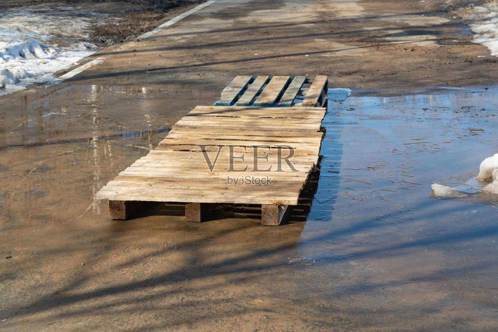 一个木制托盘桥在沥青上的水坑。照片摄影图片