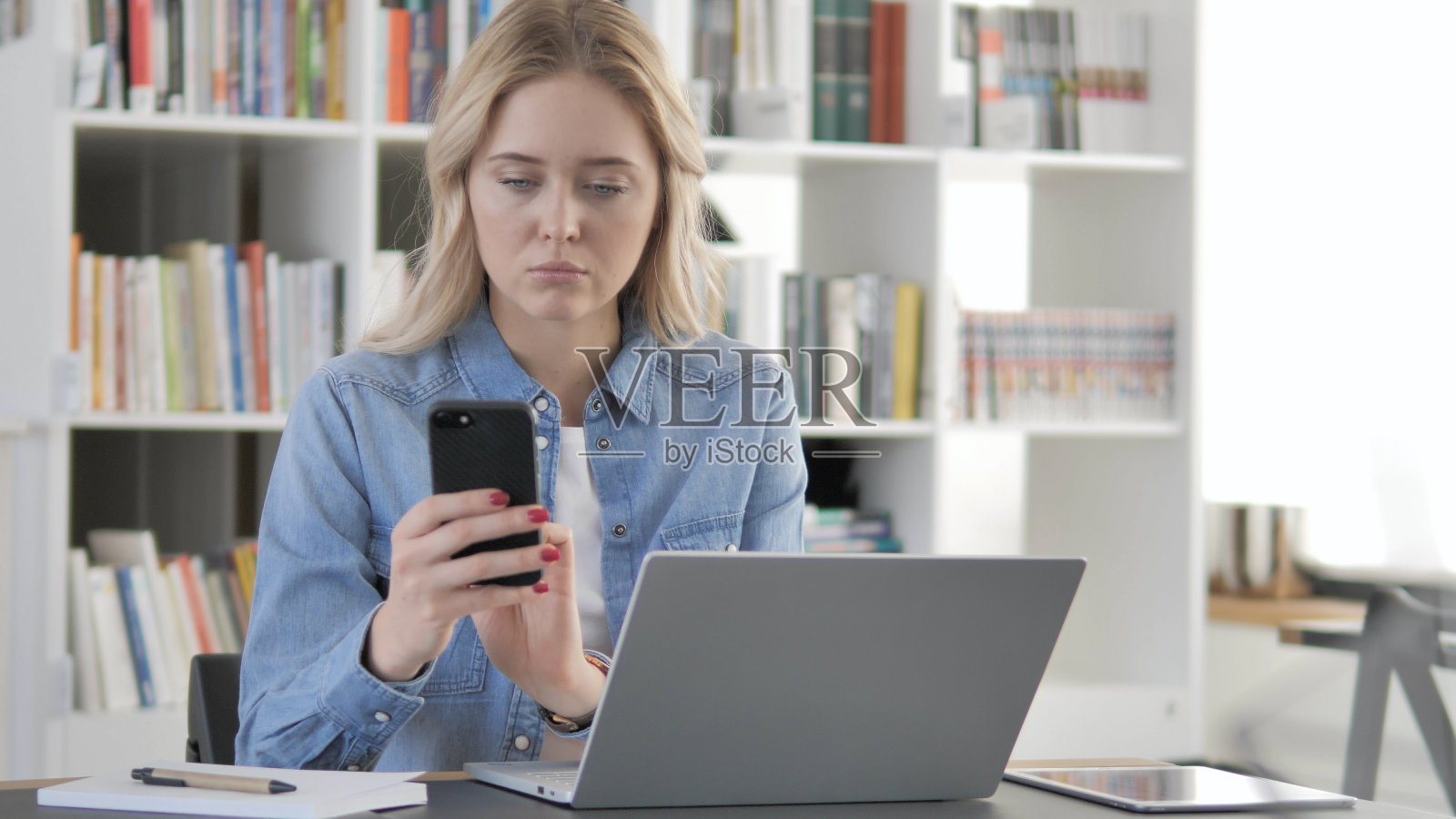 年轻的金发女子用智能手机在线工作照片摄影图片