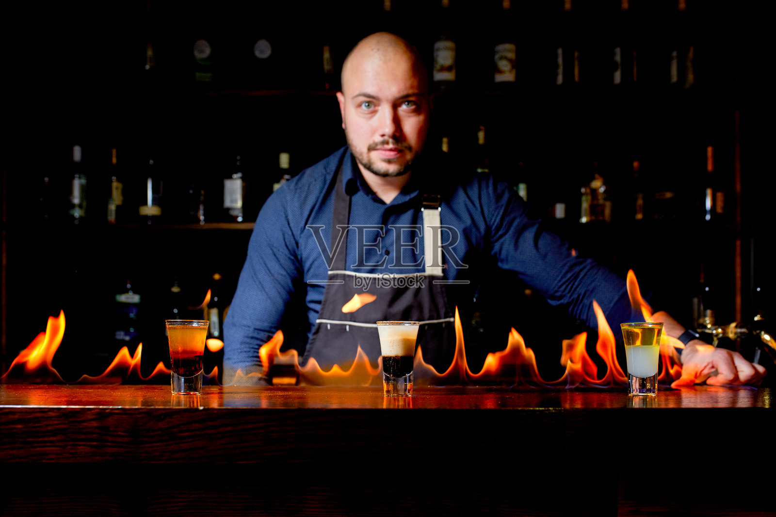 酒吧里火爆的表演。调酒师调制热酒精鸡尾酒，点燃吧台。酒保准备了烈性鸡尾酒。火在酒吧照片摄影图片