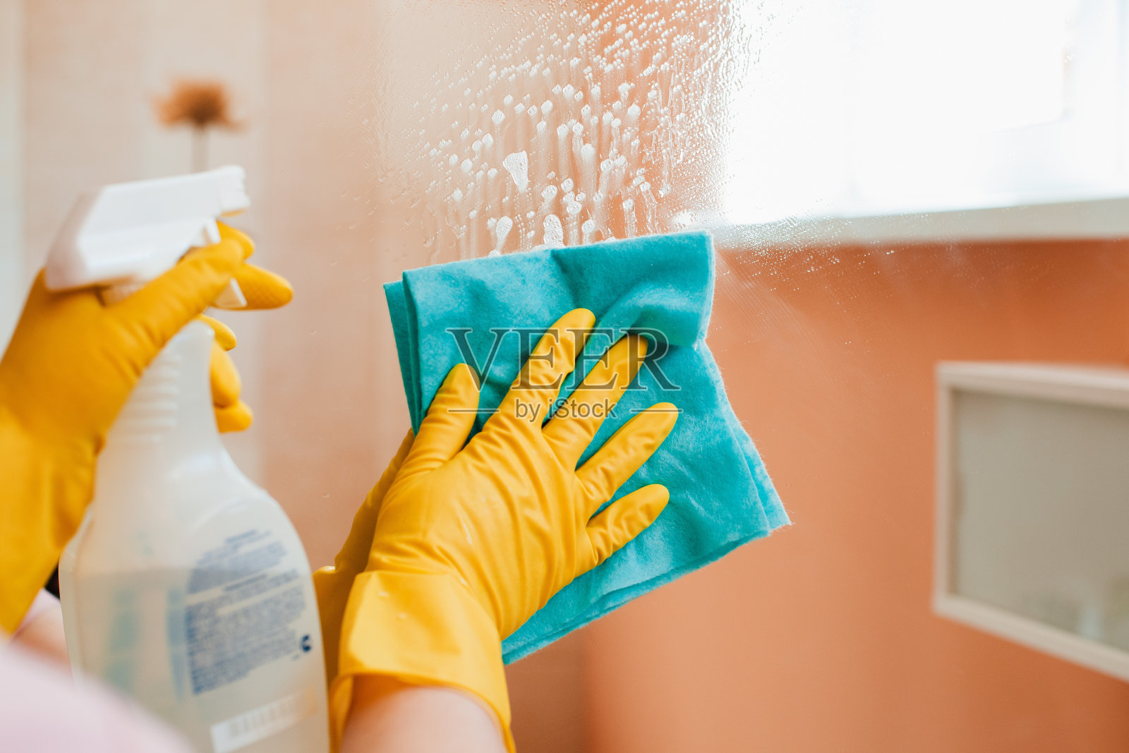 妇女在家里做家务，用泡沫海绵喷洒洗涤剂清洗镜子和窗户的表面。照片摄影图片