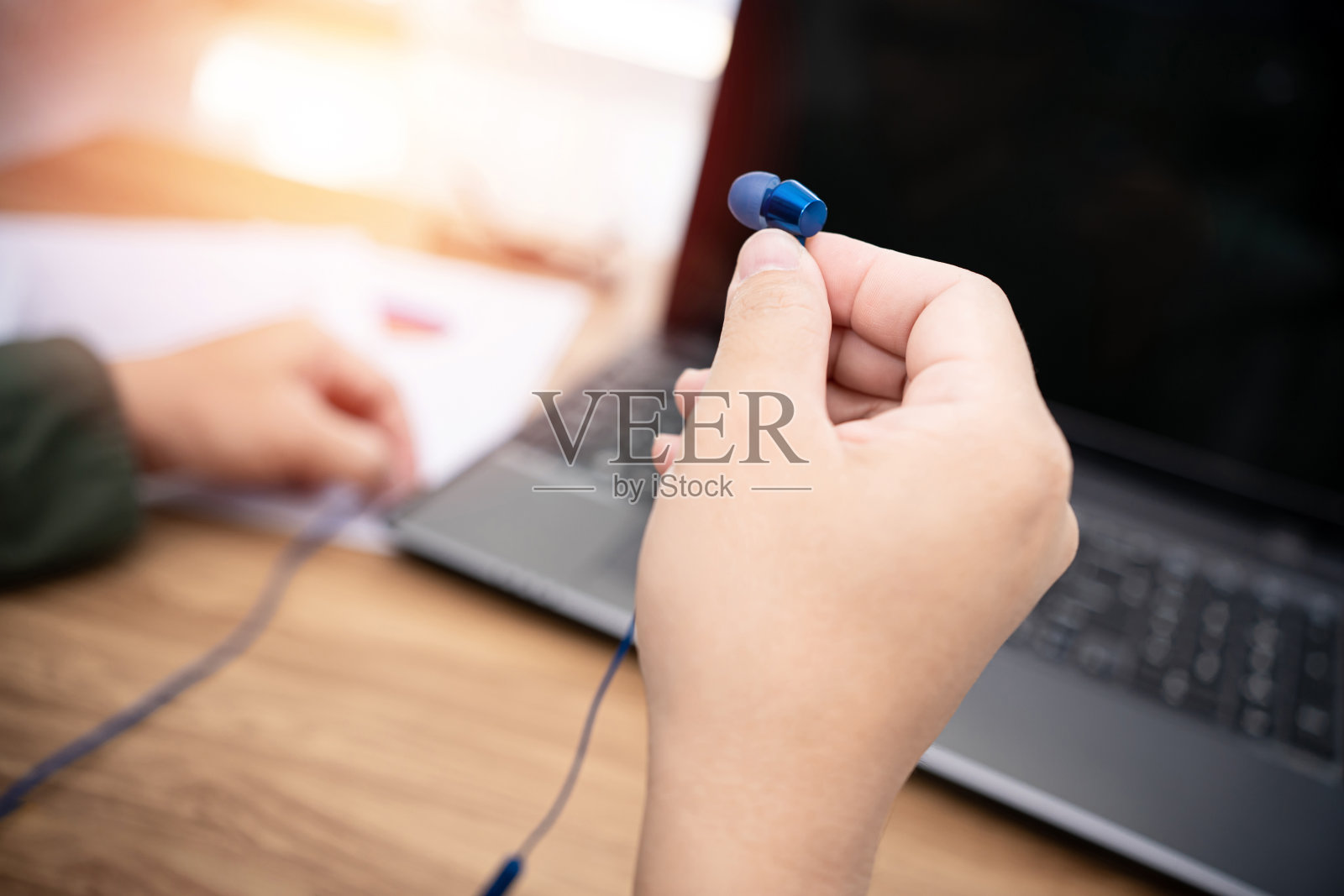 近手，一个男人拿着耳机，连接到笔记本电脑的联合工作会议在线和笔记本电脑上的工作，在家里的概念照片摄影图片