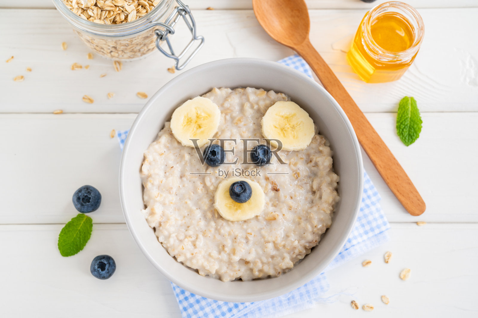 有趣的碗燕麦粥和熊脸做的水果和浆果在白色木制背景。给孩子吃的创意，俯视图，复印空间照片摄影图片
