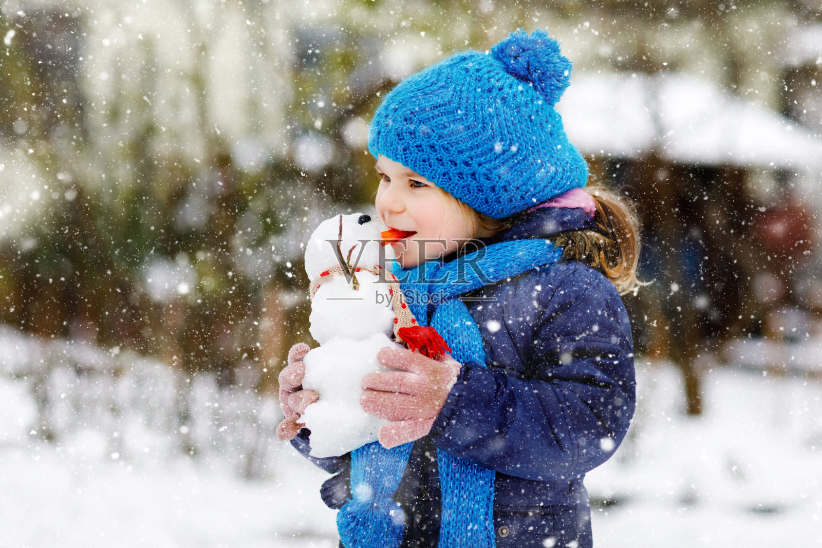 可爱的小女孩正在做迷你雪人，吃胡萝卜鼻子。可爱健康快乐的孩子在雪地里玩耍，在寒冷的日子里在户外玩耍。与孩子们在冬季积极休闲照片摄影图片
