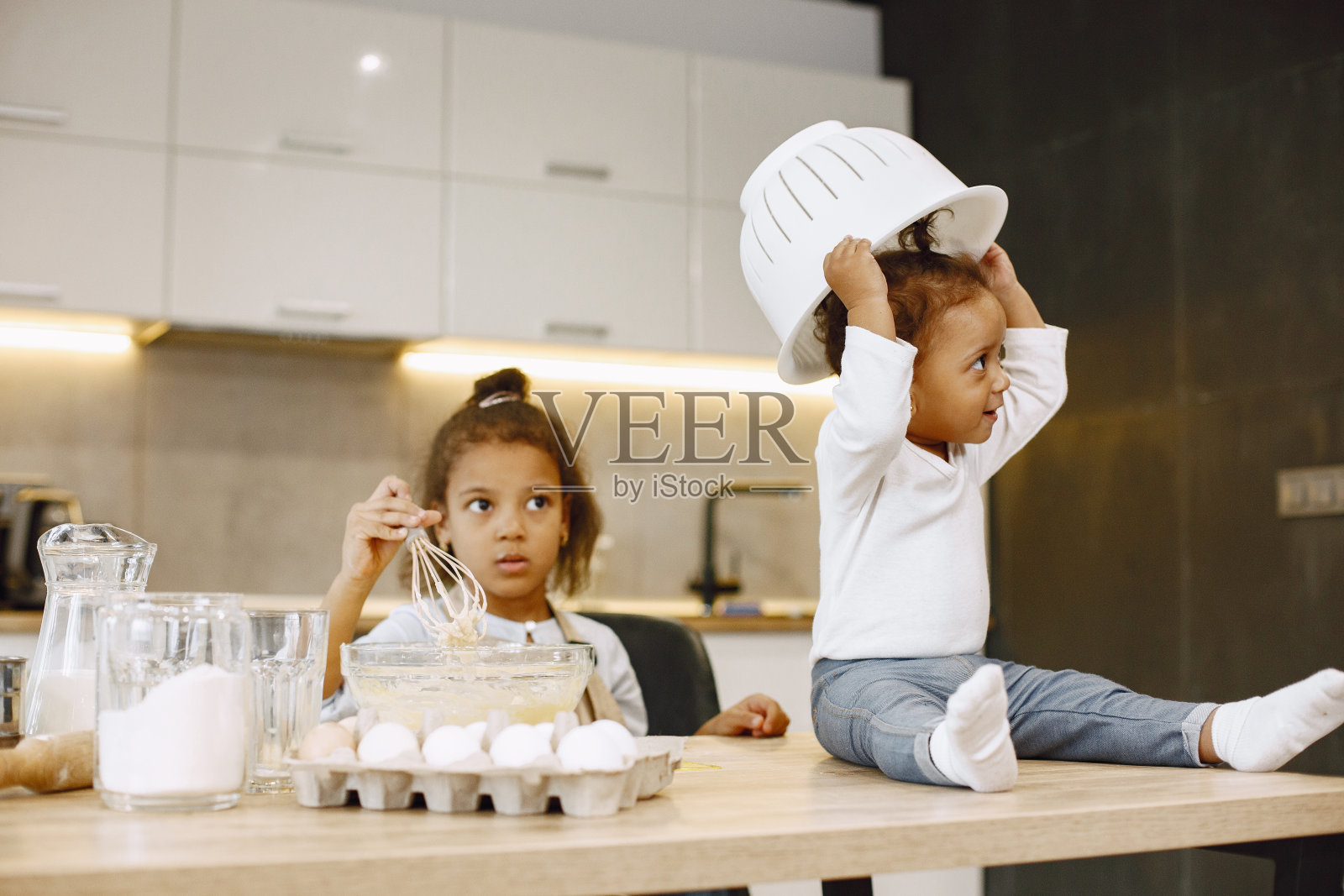 两个孩子在厨房里。拿着面团的小女孩。穿着米色围裙的孩子照片摄影图片