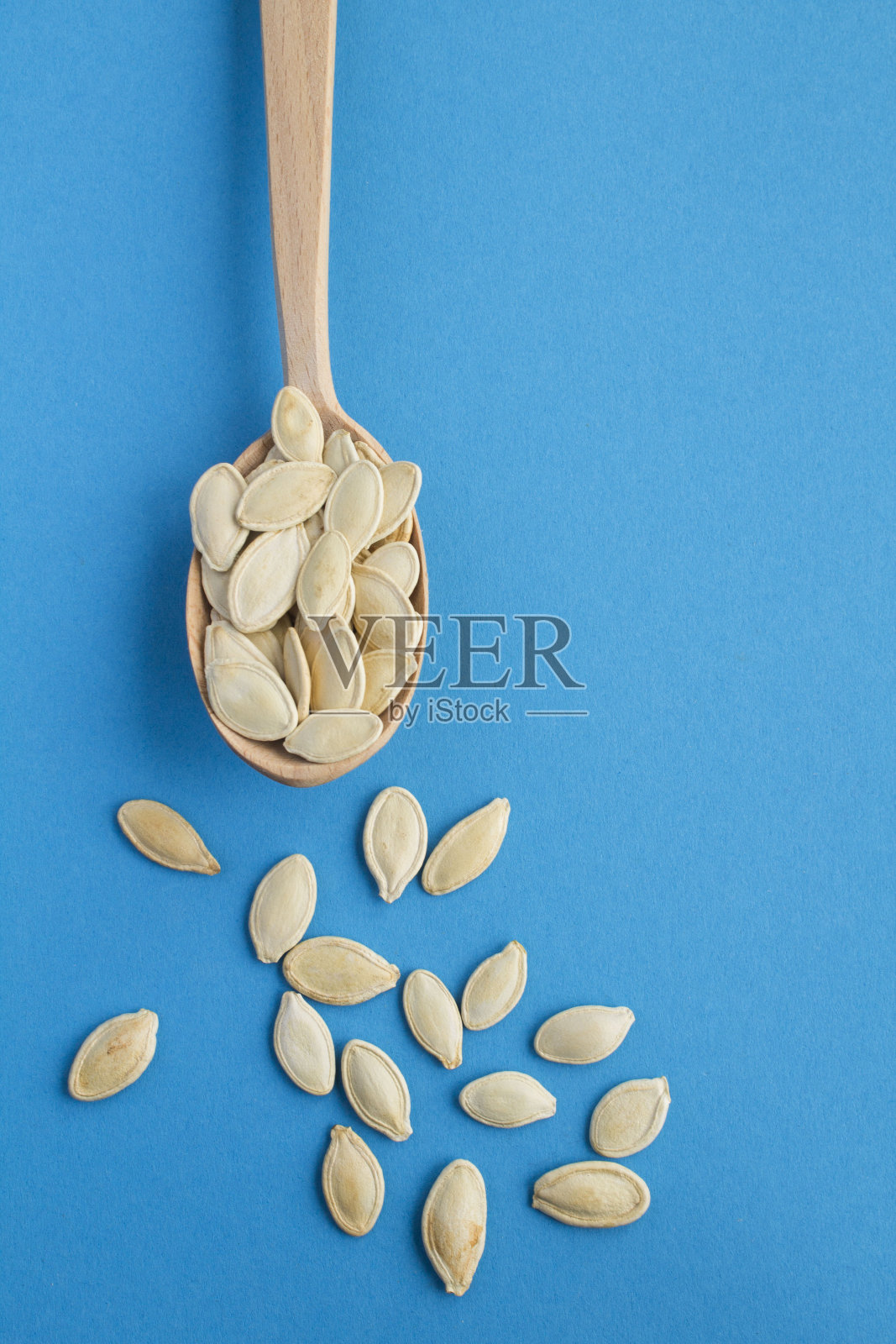蓝色背景上木勺里的南瓜籽。副本的空间。前视图。照片摄影图片