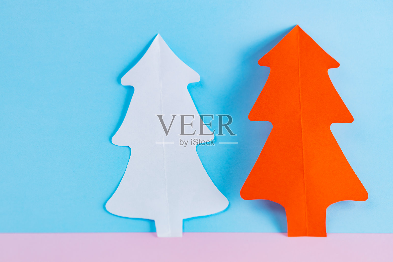 蓝色粉红色背景上的纸圣诞树。白色和红色的纸圣诞树。圣诞节最小的概念照片摄影图片