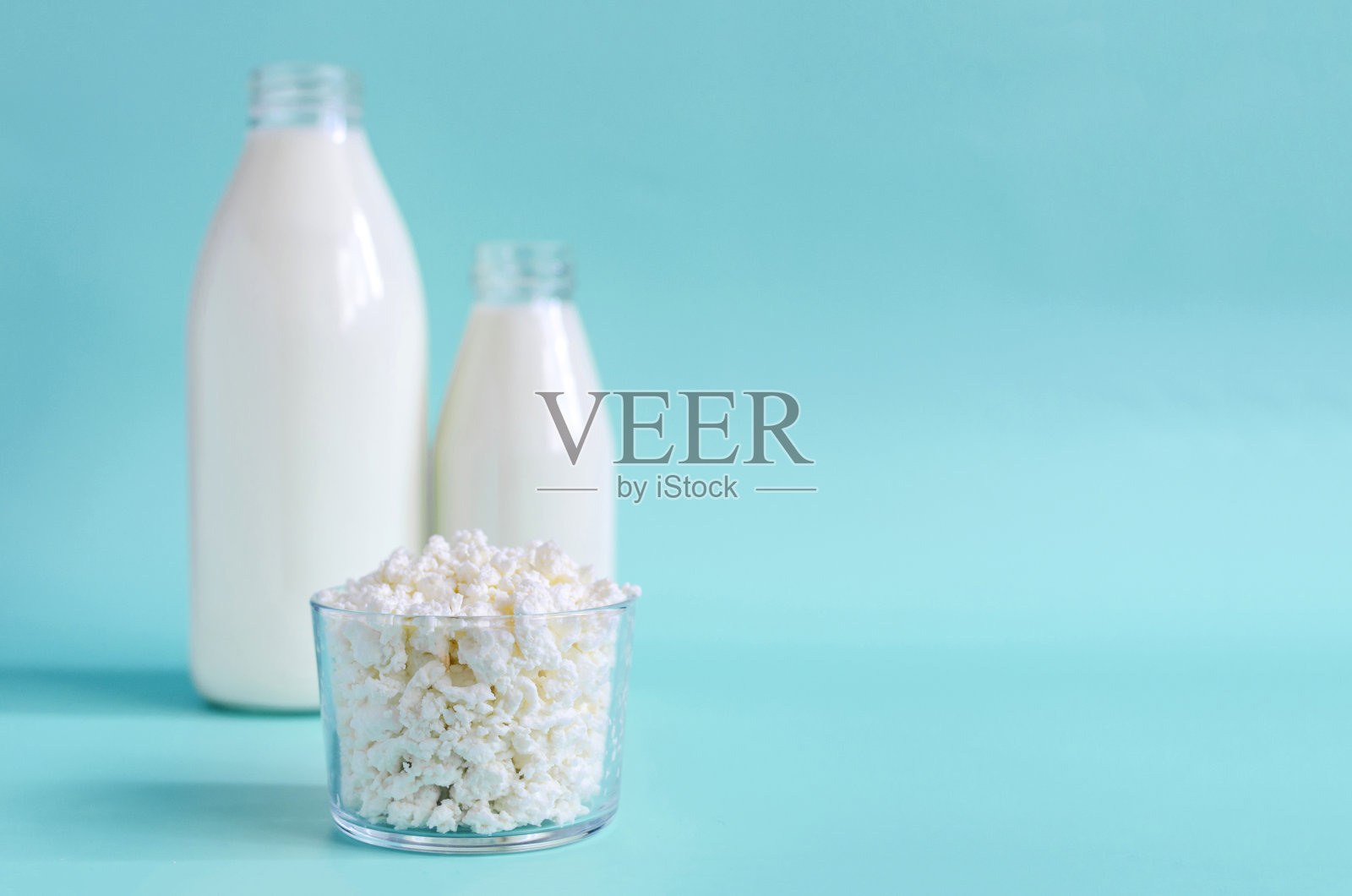 新鲜的白软干酪在一个玻璃容器的背景牛奶瓶，锐利在前景。松软干酪放在一个透明的盘子里，在浅色背景上放上文字照片摄影图片